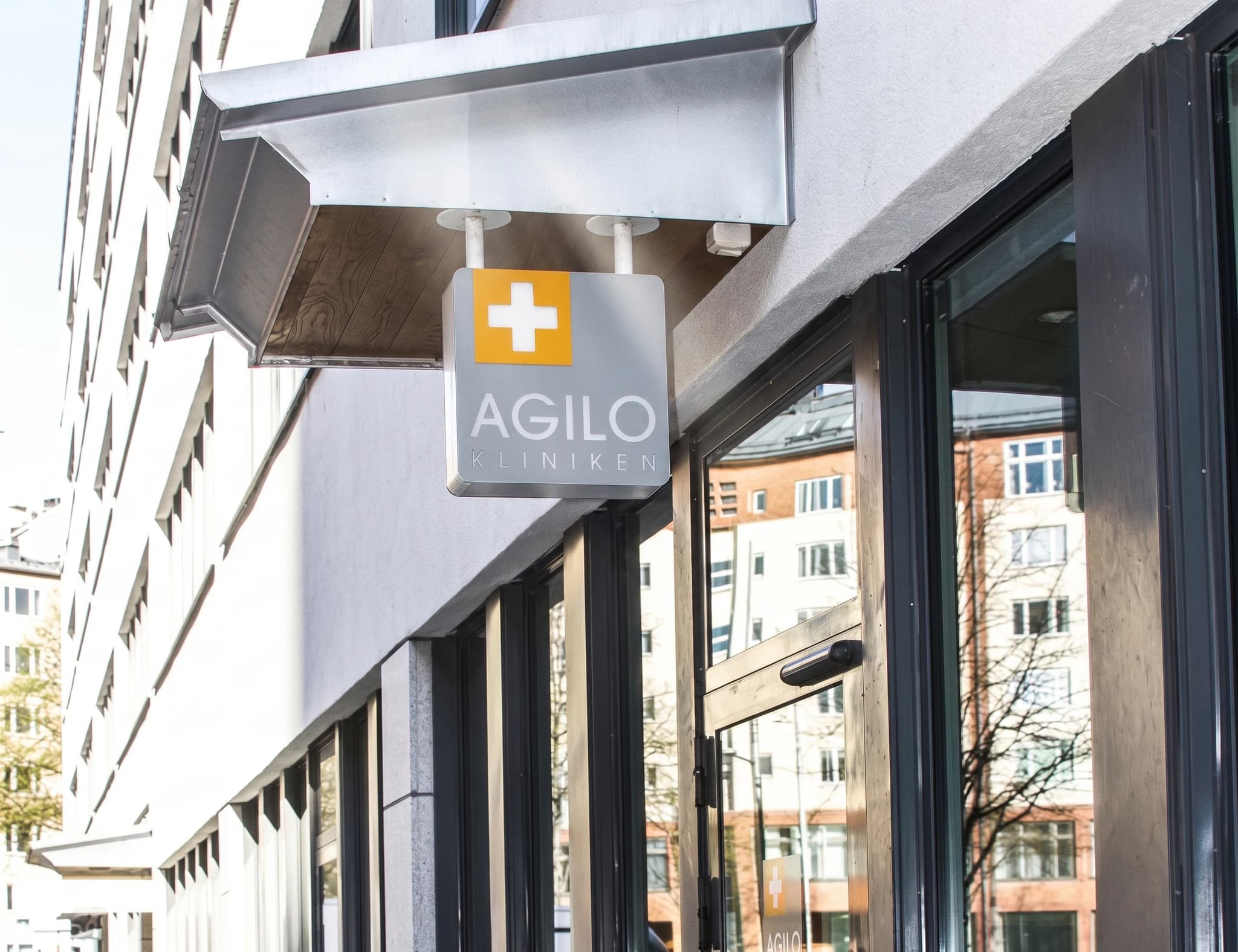 En skylt för Agilo kliniken hänger utanför en byggnad med stora fönster.