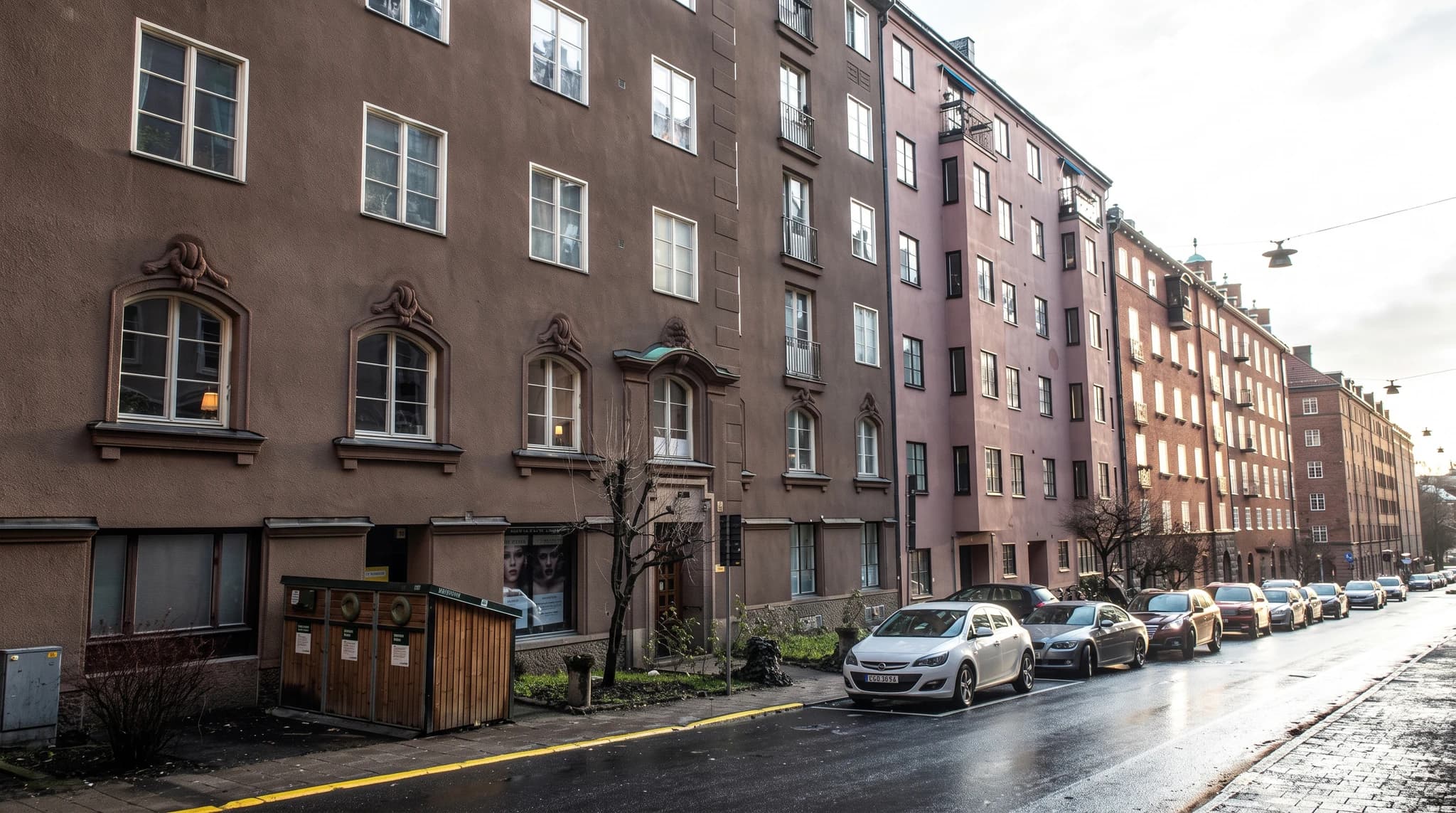Exteriörbild av brun och ljusrosa flerfamiljshus med bilar parkerade längs gatan.