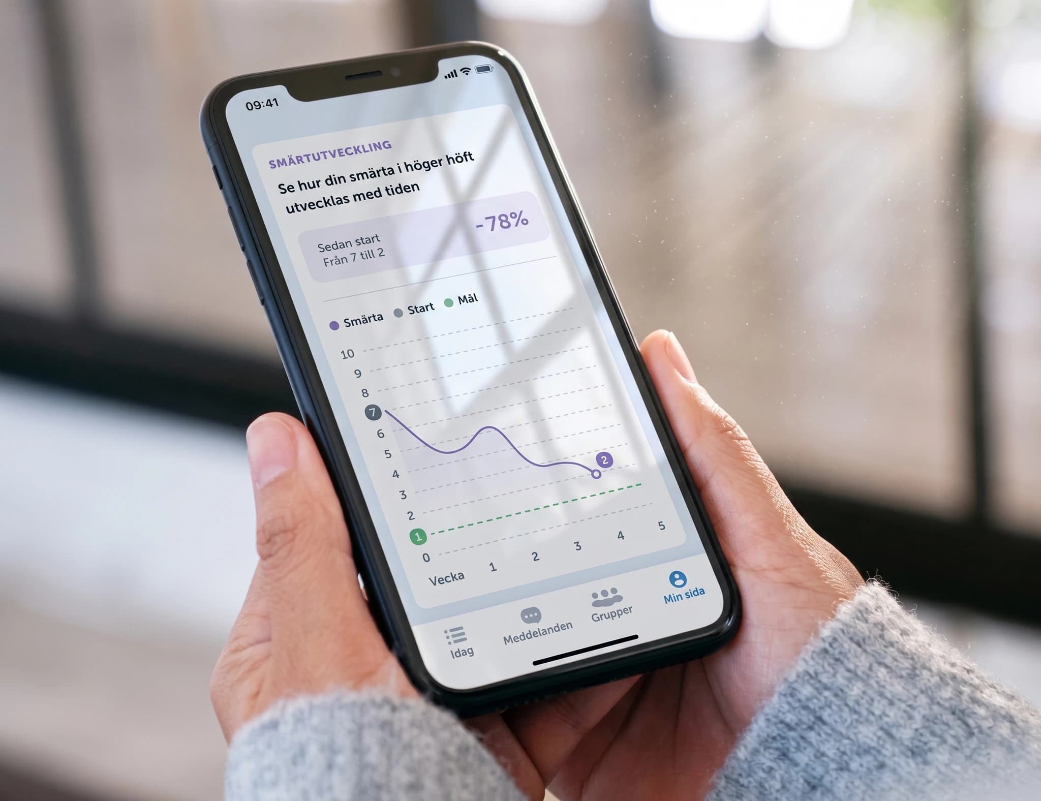 En person håller en smartphone som visar en app för smärtutveckling med en graf som visar smärtnivåer över tid.