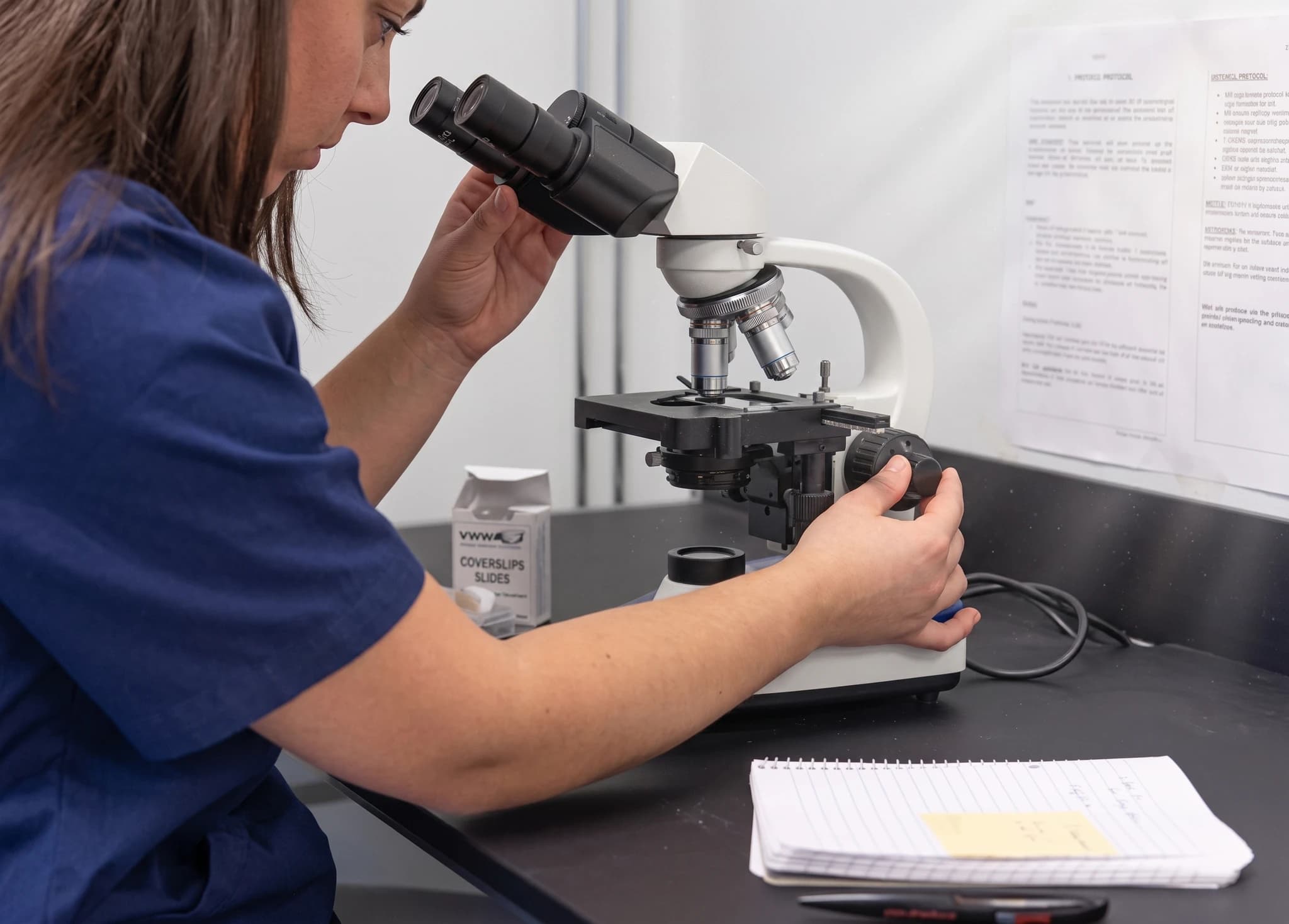 Sjuksköterska undersöker prov under mikroskop i ett laboratorium.