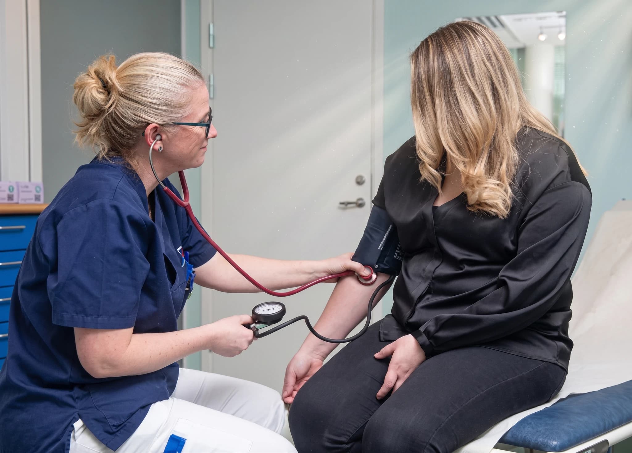 Sjuksköterska tar blodtryck på patient i undersökningsrum.