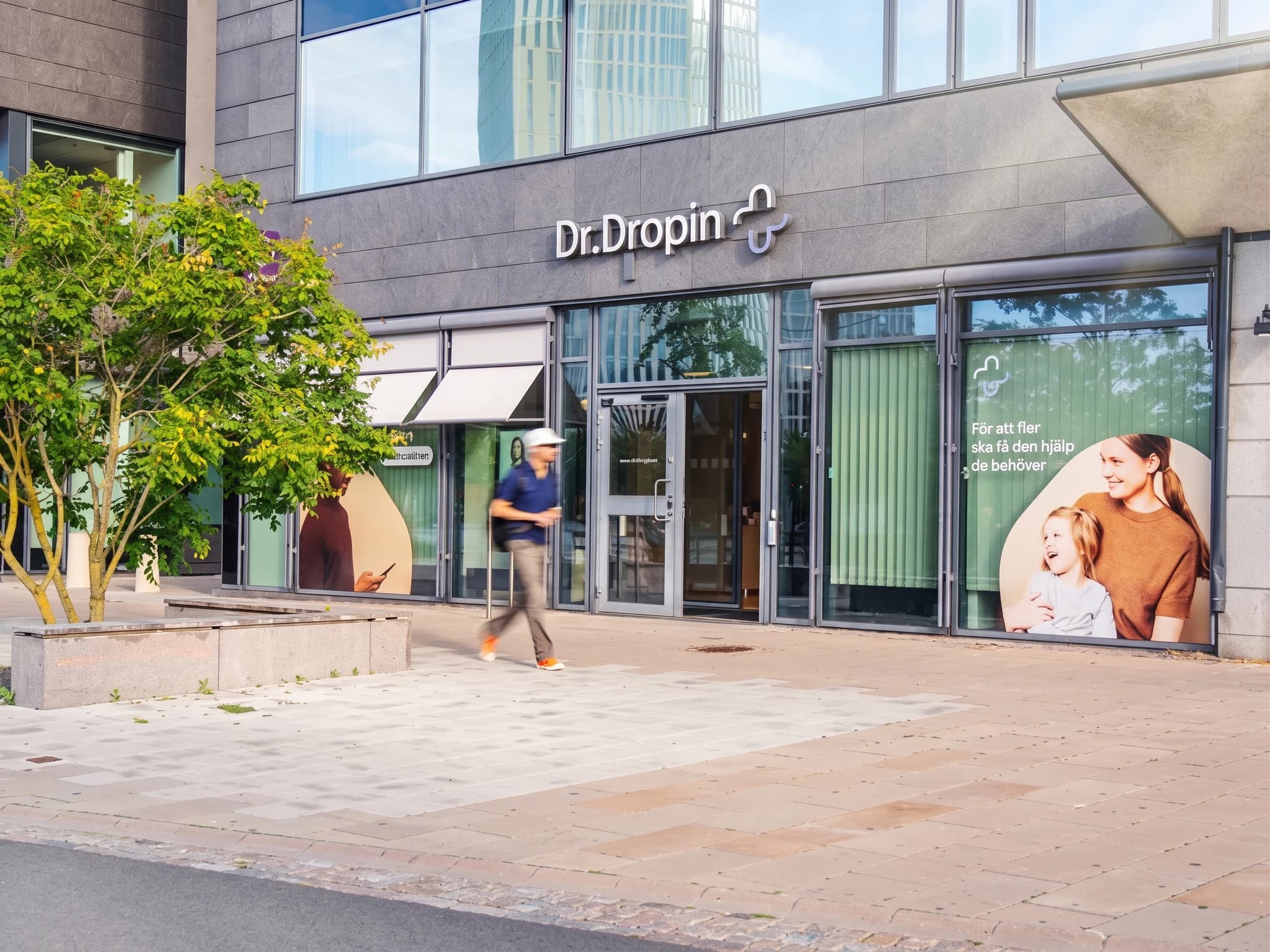 Exteriör av en klinik med logotypen Dr. Dropin, en man går förbi på trottoaren och reklambilder visas i fönstren.