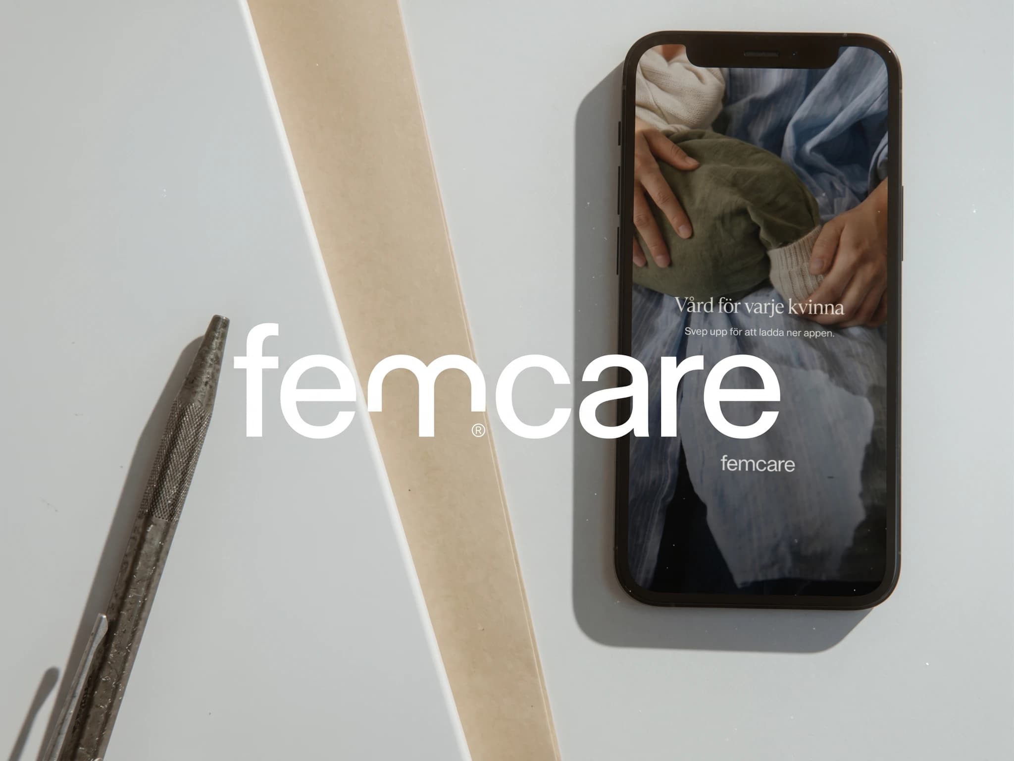 Femcare logotypen på en mobiltelefonskärm med appens gränssnitt, bredvid en sax och ett band.