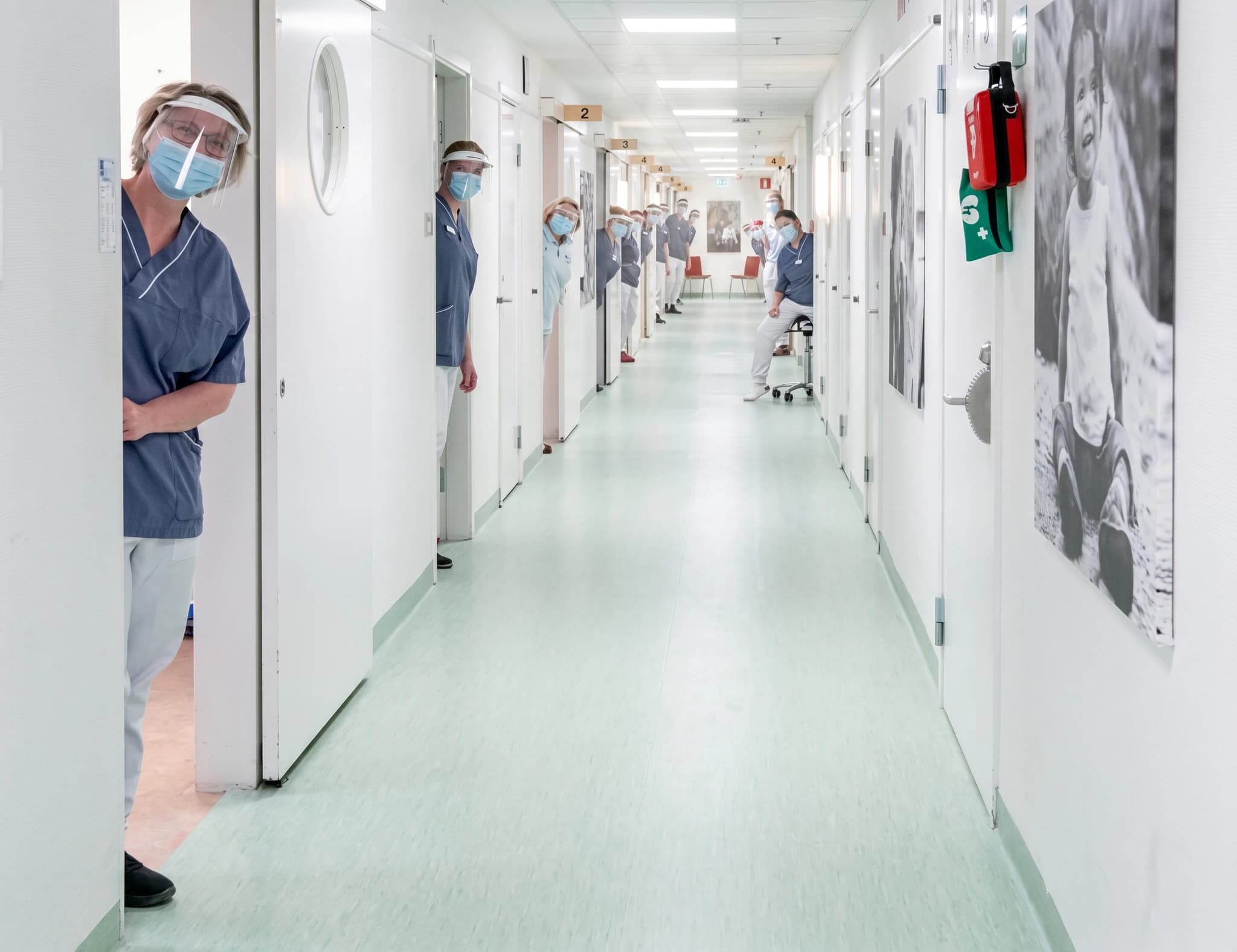 Medicinsk personal som kikar fram från dörröppningar i en sjukhuskorridor.