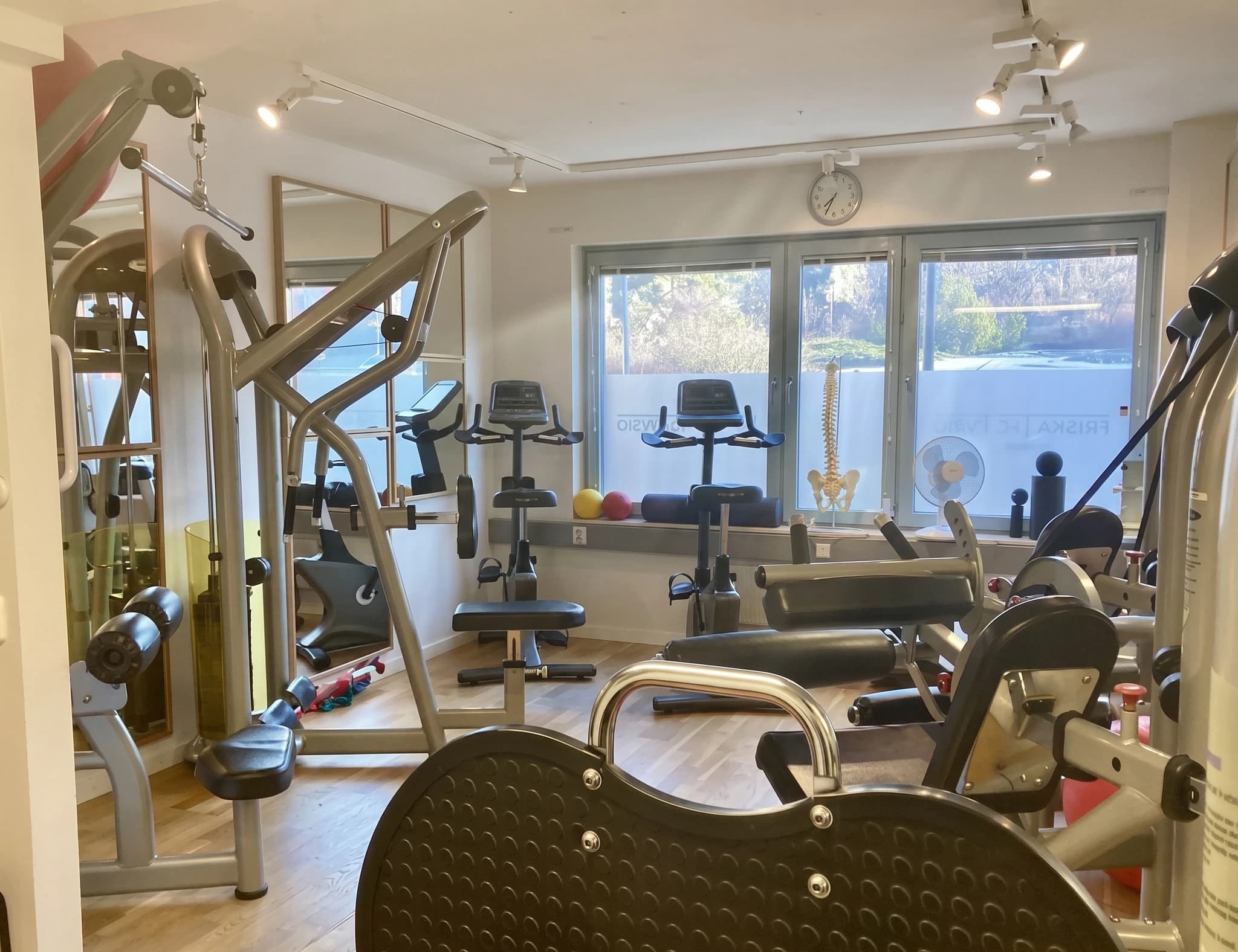 Olika träningsmaskiner och redskap i ett rehabiliteringsrum eller gym, inklusive en stående cykel och en benpress.
