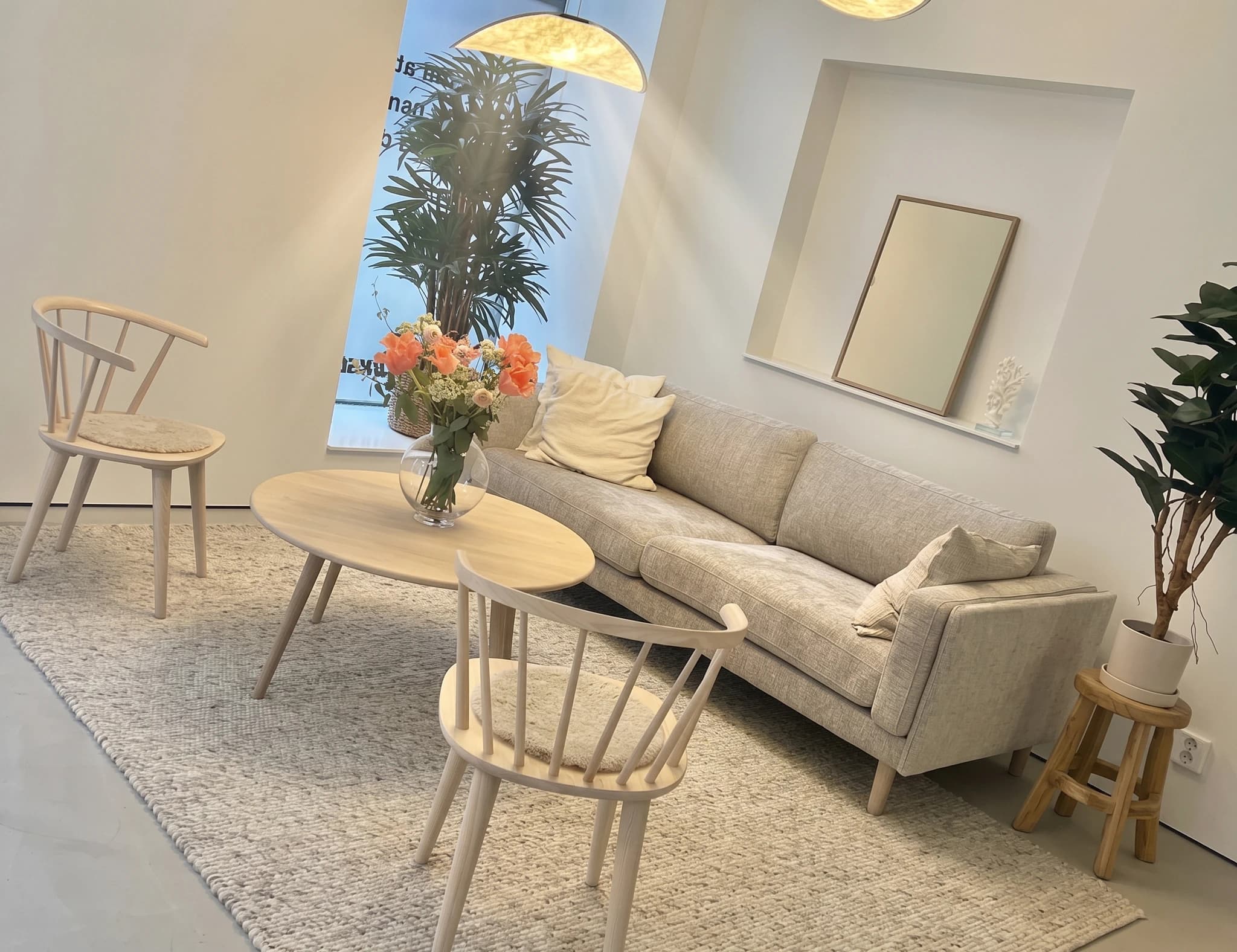 Modern lounge med ljus soffa, trästolar och ett runt soffbord med en vas blommor.
