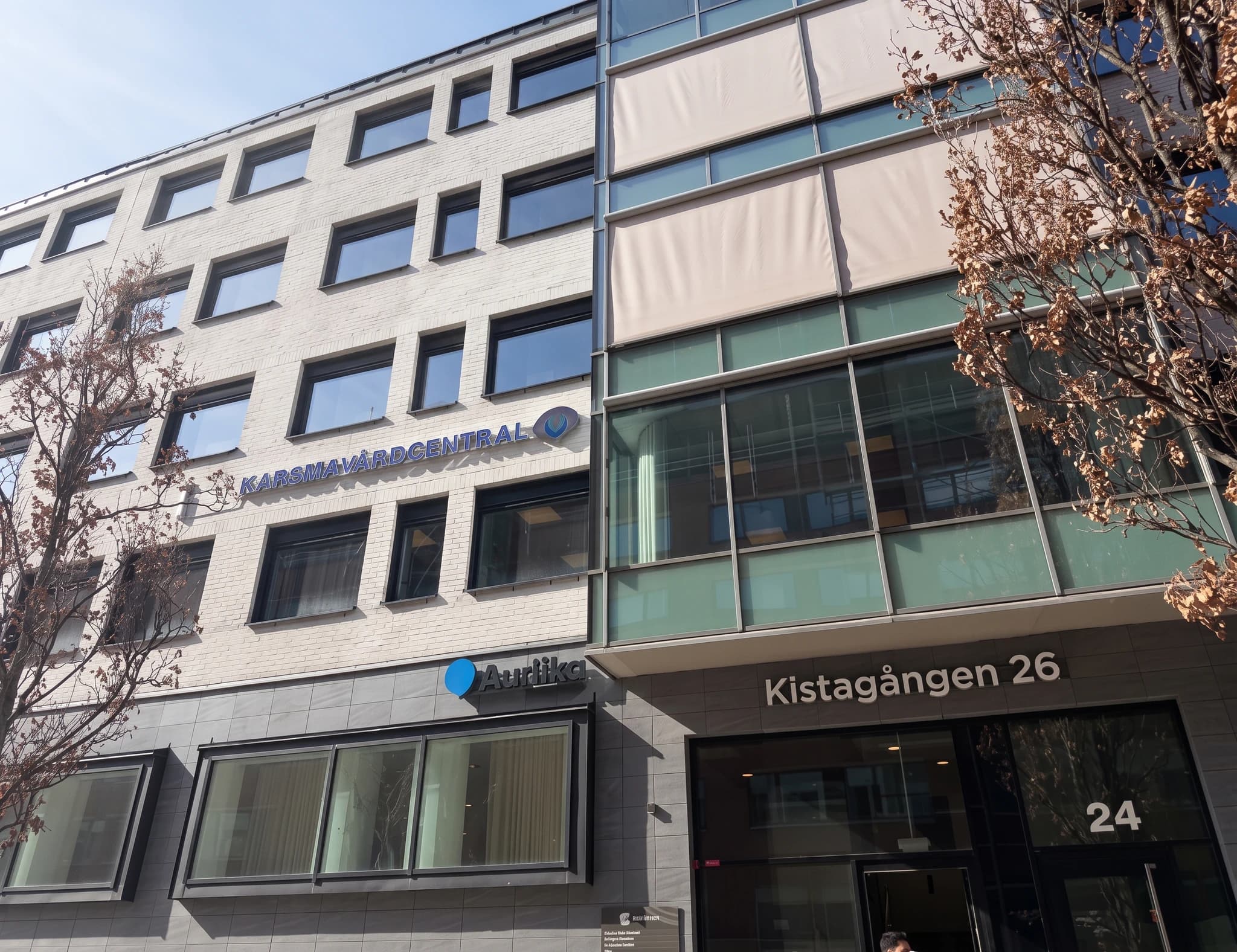Exteriör av Kistagången 26-byggnaden med skyltar, inklusive Kassa- och Vårcentralen och "Audilika".