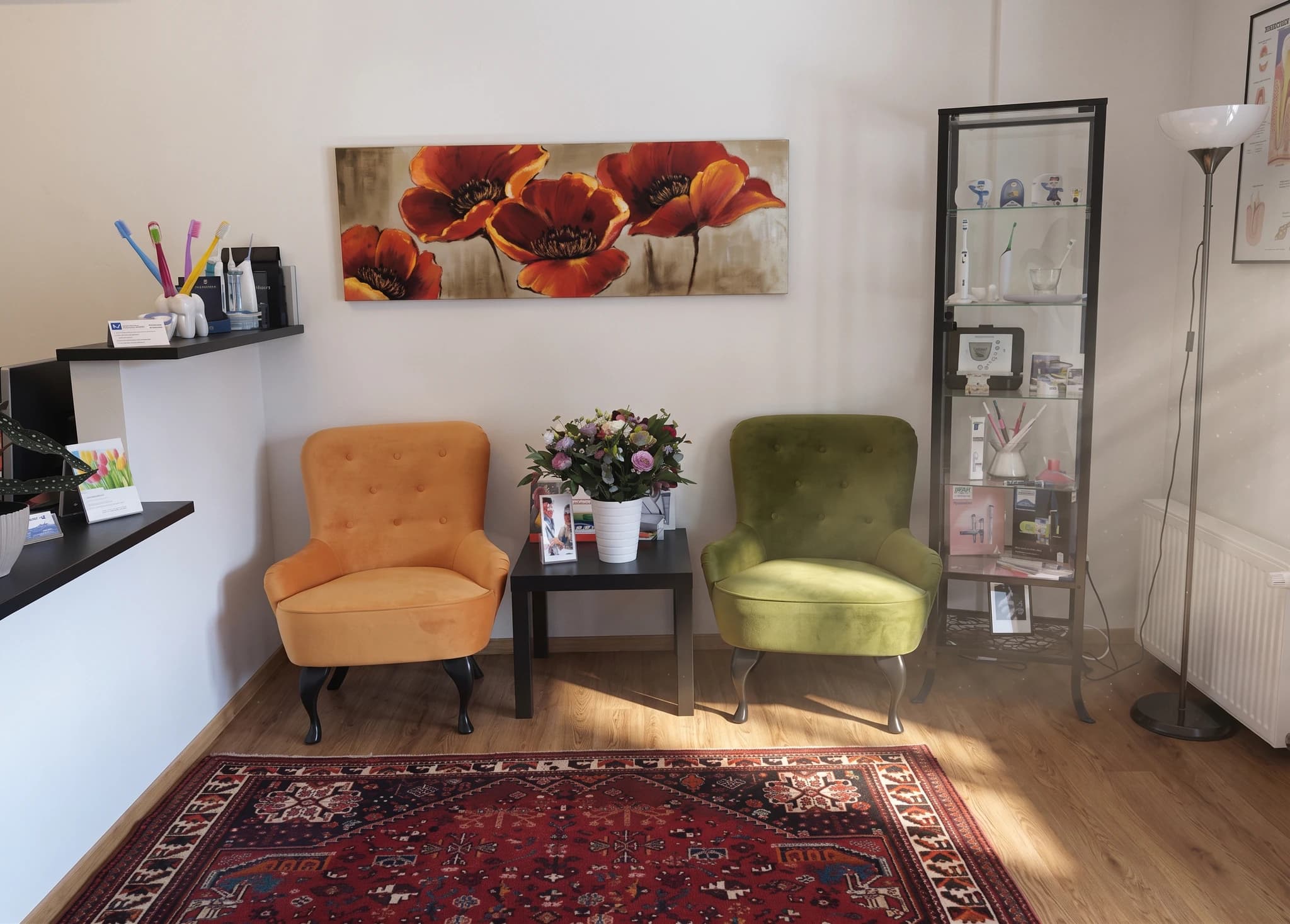 En väntrumsmiljö med en gul och en grön fåtölj som står mitt emot varandra, med ett litet svart bord med en blomsterbukett emellan. Till höger finns ett högt vitrinskåp med utställda föremål.