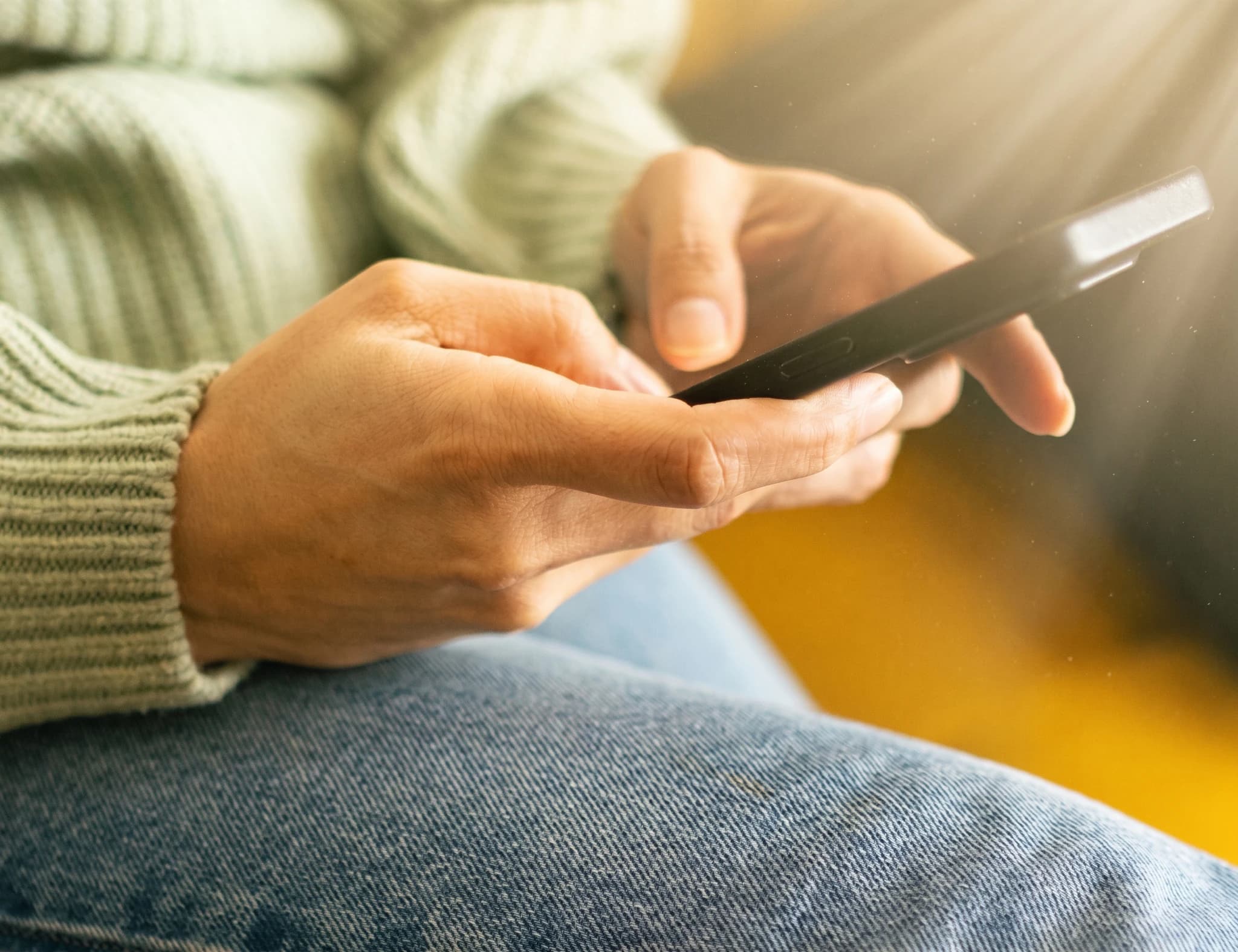 Händerna av en person som använder en smartphone, med den nedre delen av kroppen klädd i jeans.