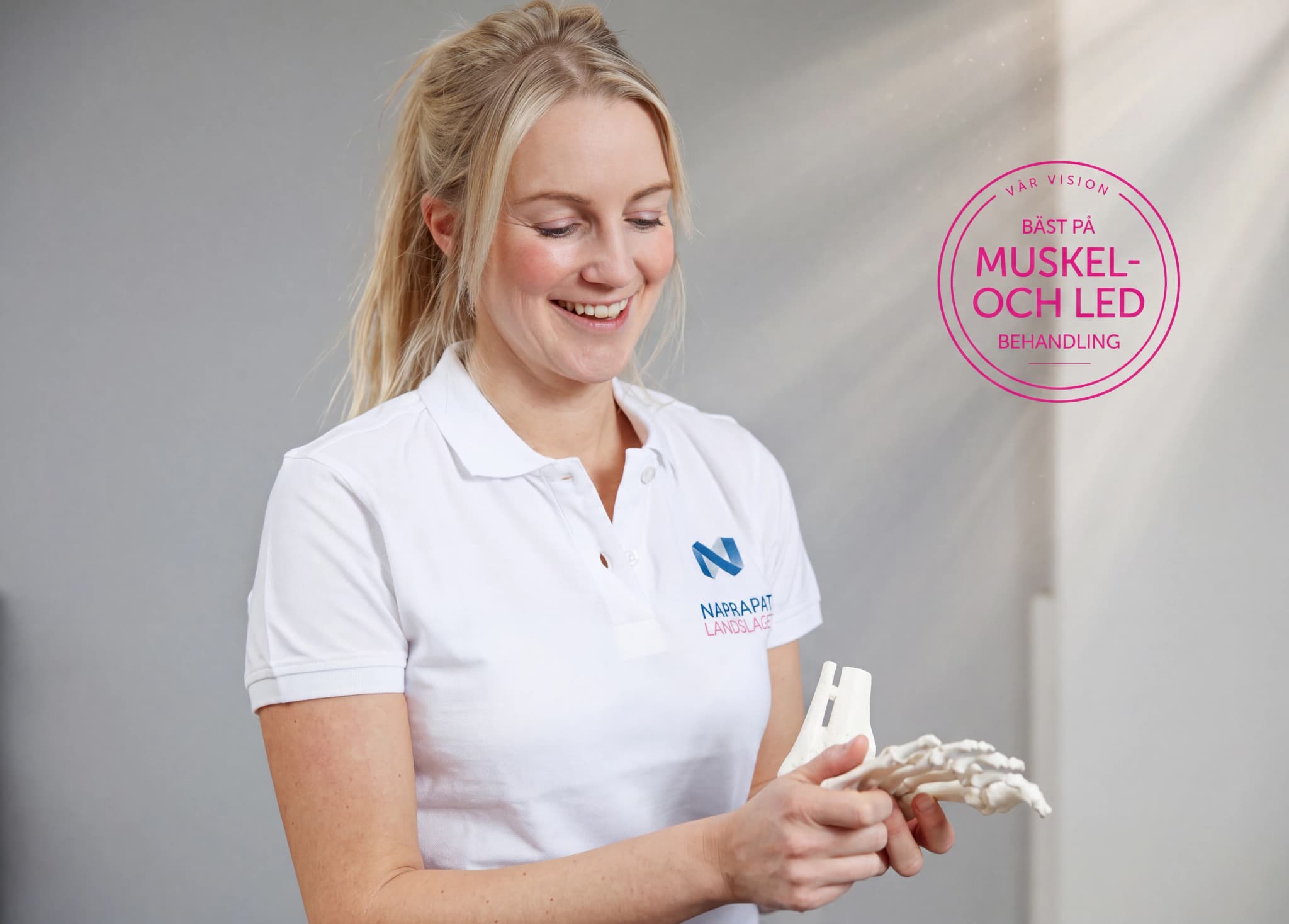 En fysioterapeut ler medan hon håller upp en modell av en fot och visar dess anatomi.
