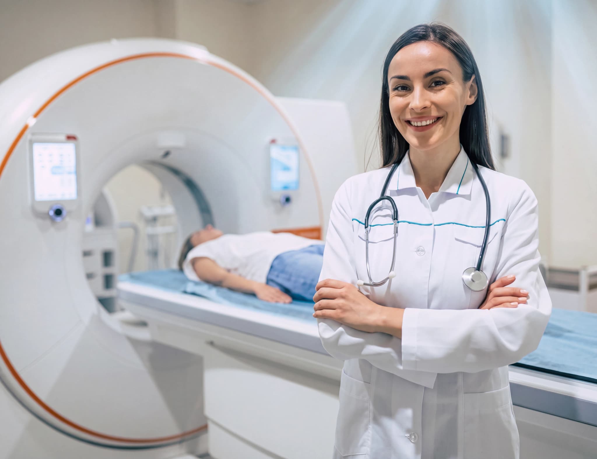 Läkare med stetoskop runt halsen står med korslagda armar framför en CT-scanner där en patient ligger på britsen.