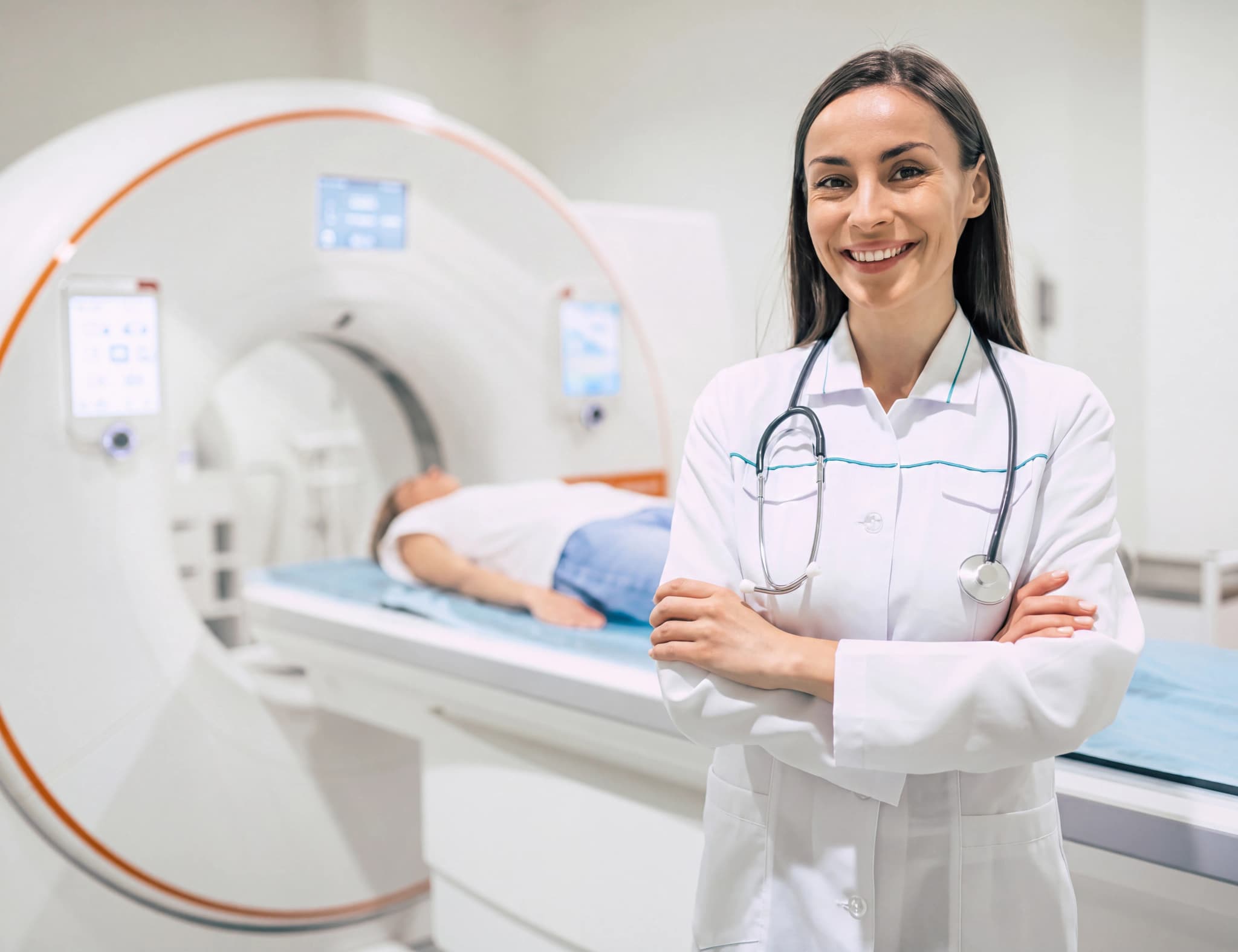 En leende läkare står framför en MRI-skanner där en patient ligger på bordet.