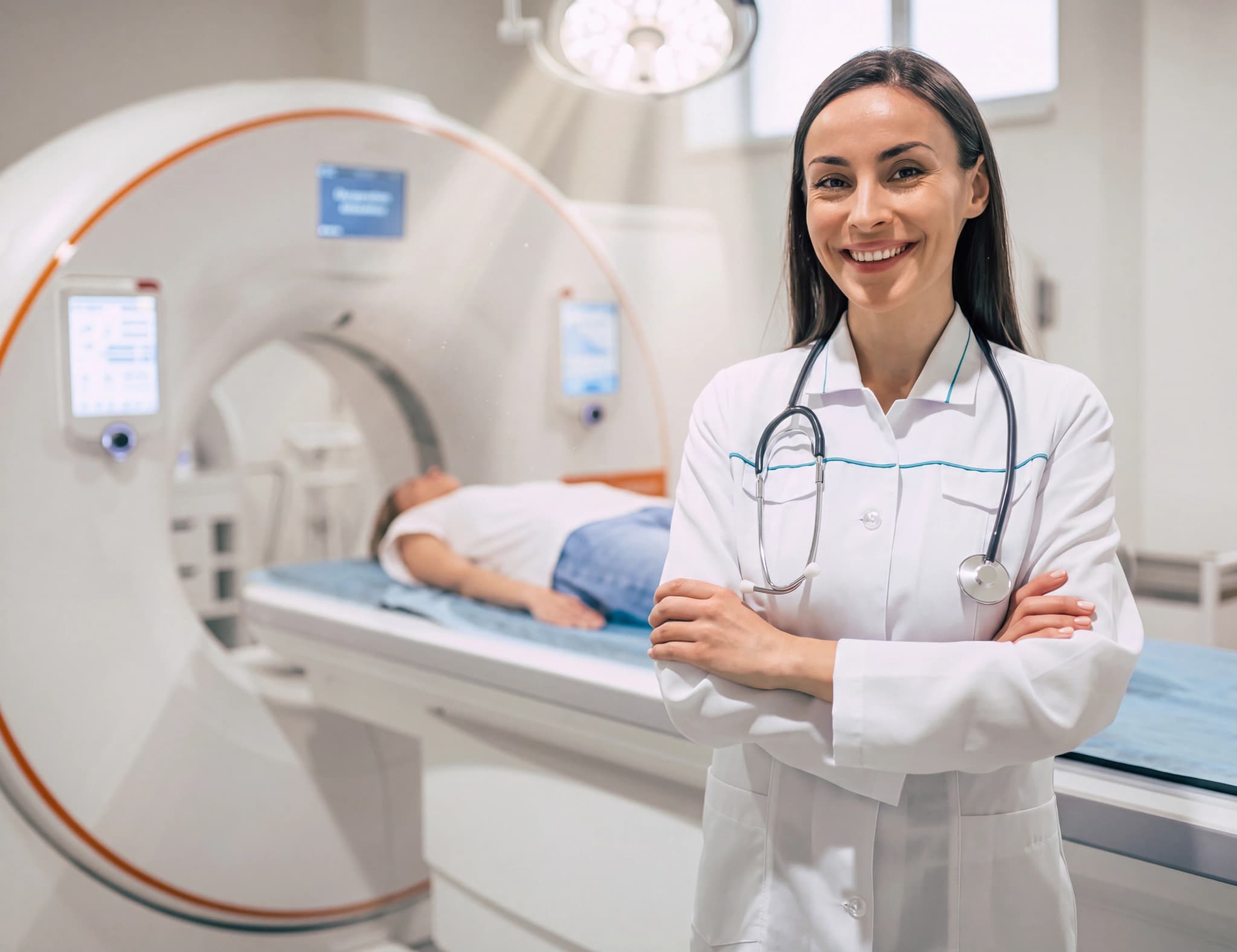 Radiolog i vit rock med stetoskop ler med armarna i kors framför en CT-scanningsmaskin där en patient ligger på britsen.