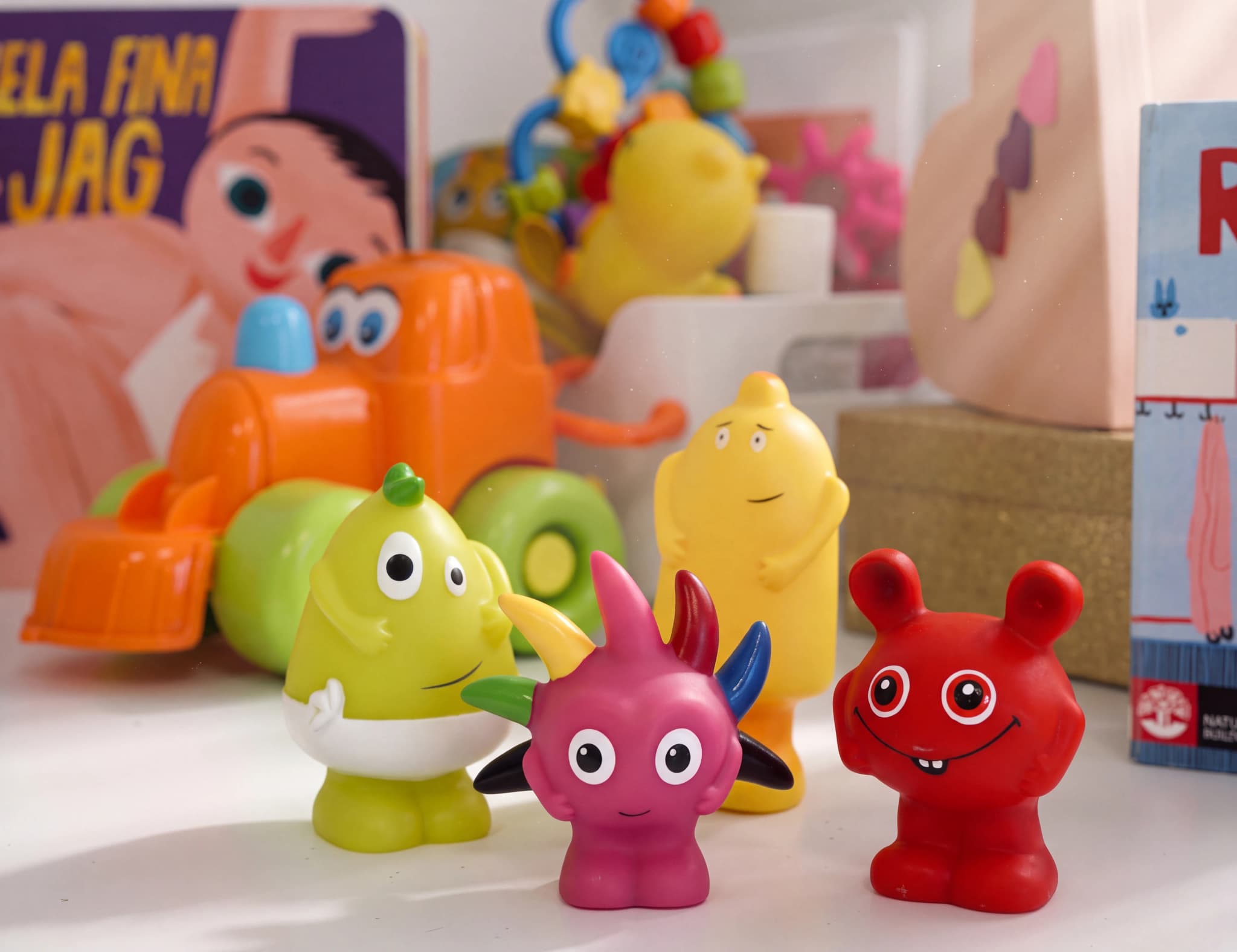 En samling färgglada leksaker för små barn, inklusive figurer, en leksaksbil och en babymonitor, arrangerade på en hylla.