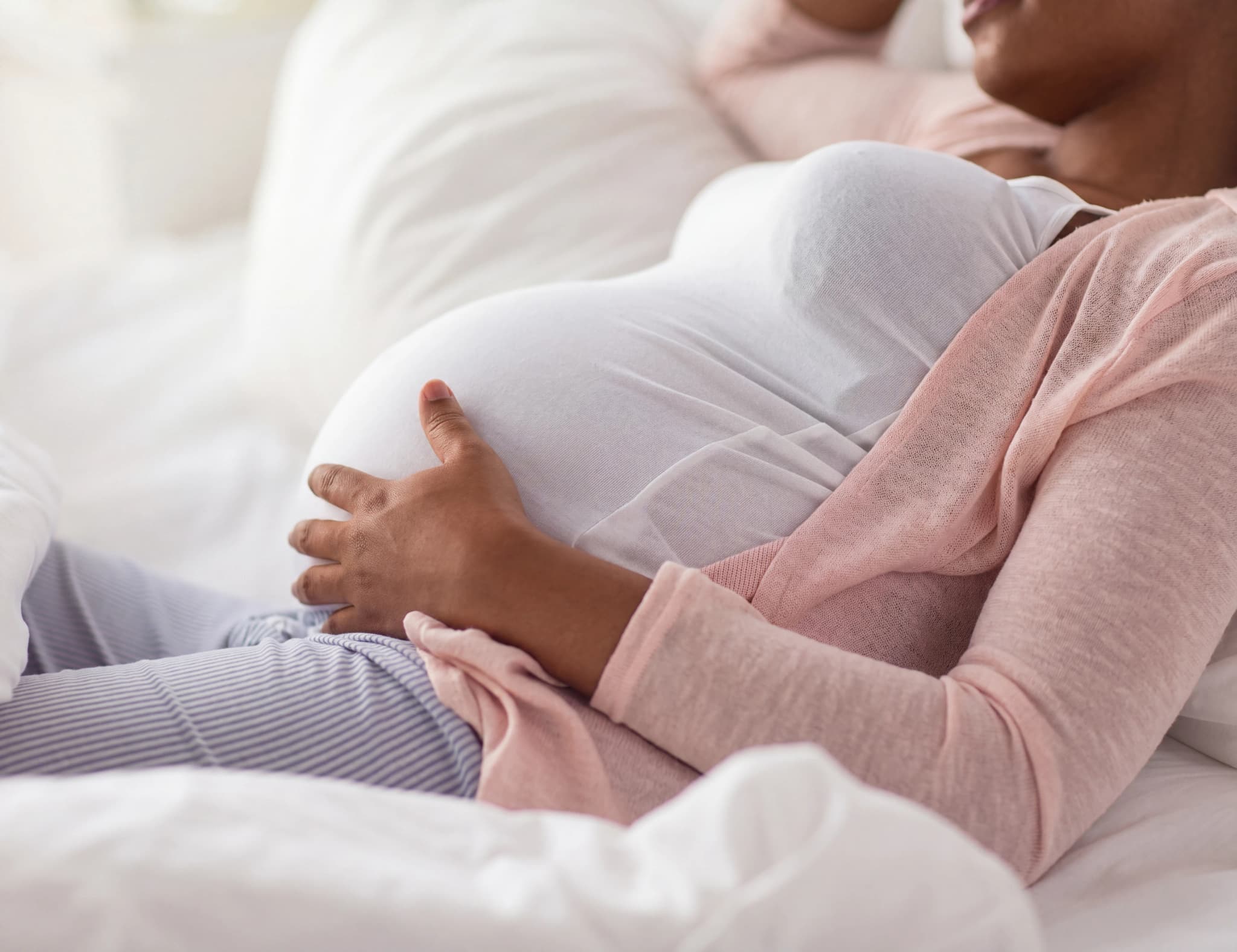 Gravid kvinna med handen på magen som vilar på en säng.