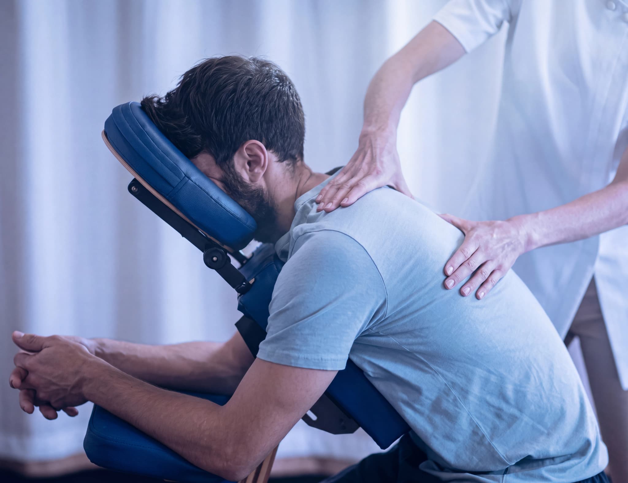 Massageterapeut masserar en mans rygg medan han sitter i en massagestol.