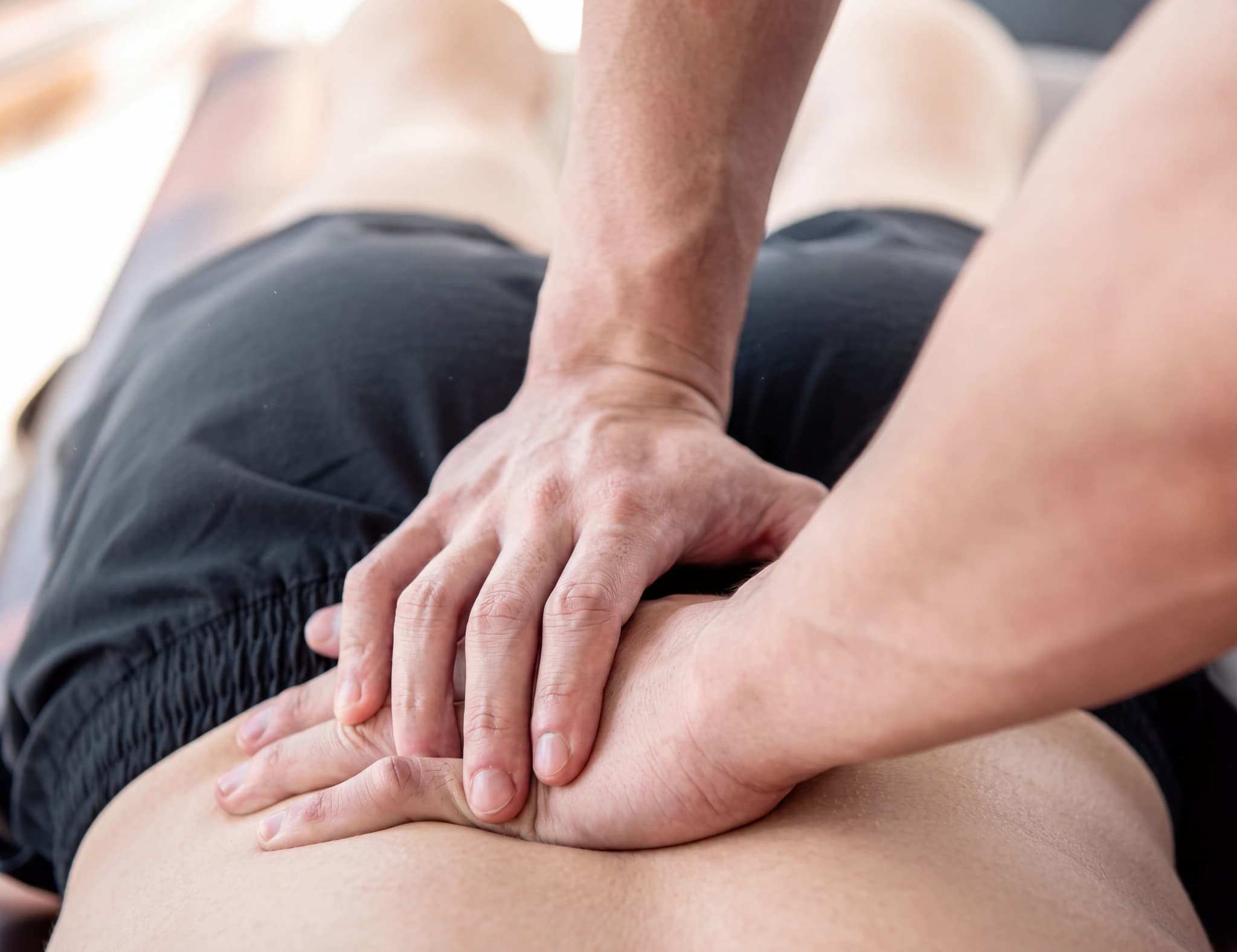 En massageterapeut masserar en patients nedre rygg med båda händerna.