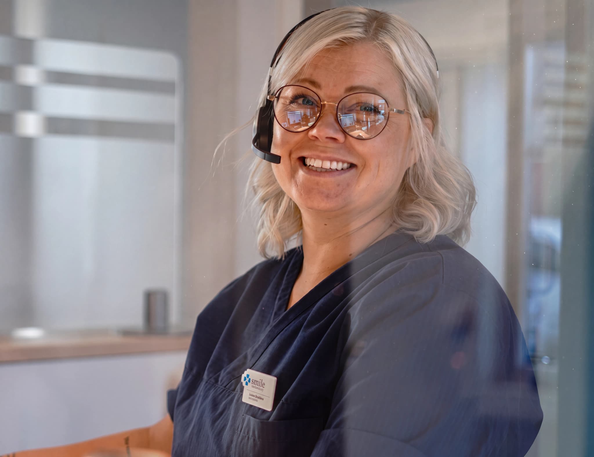 En receptionist med headset ler mot kameran vid ett receptionsdisk.