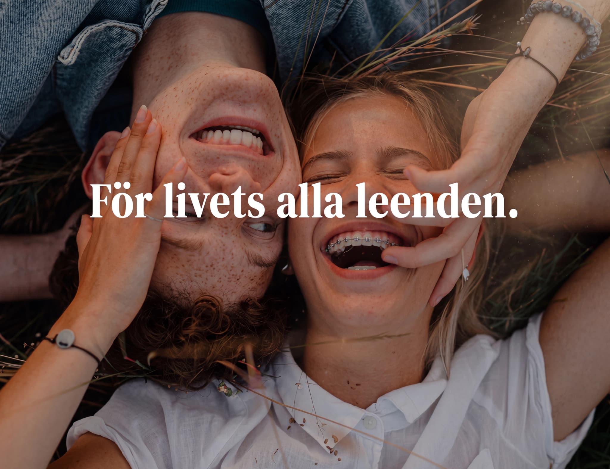 Ungt par ligger ner utomhus och skrattar, med texten "För livets alla leenden."