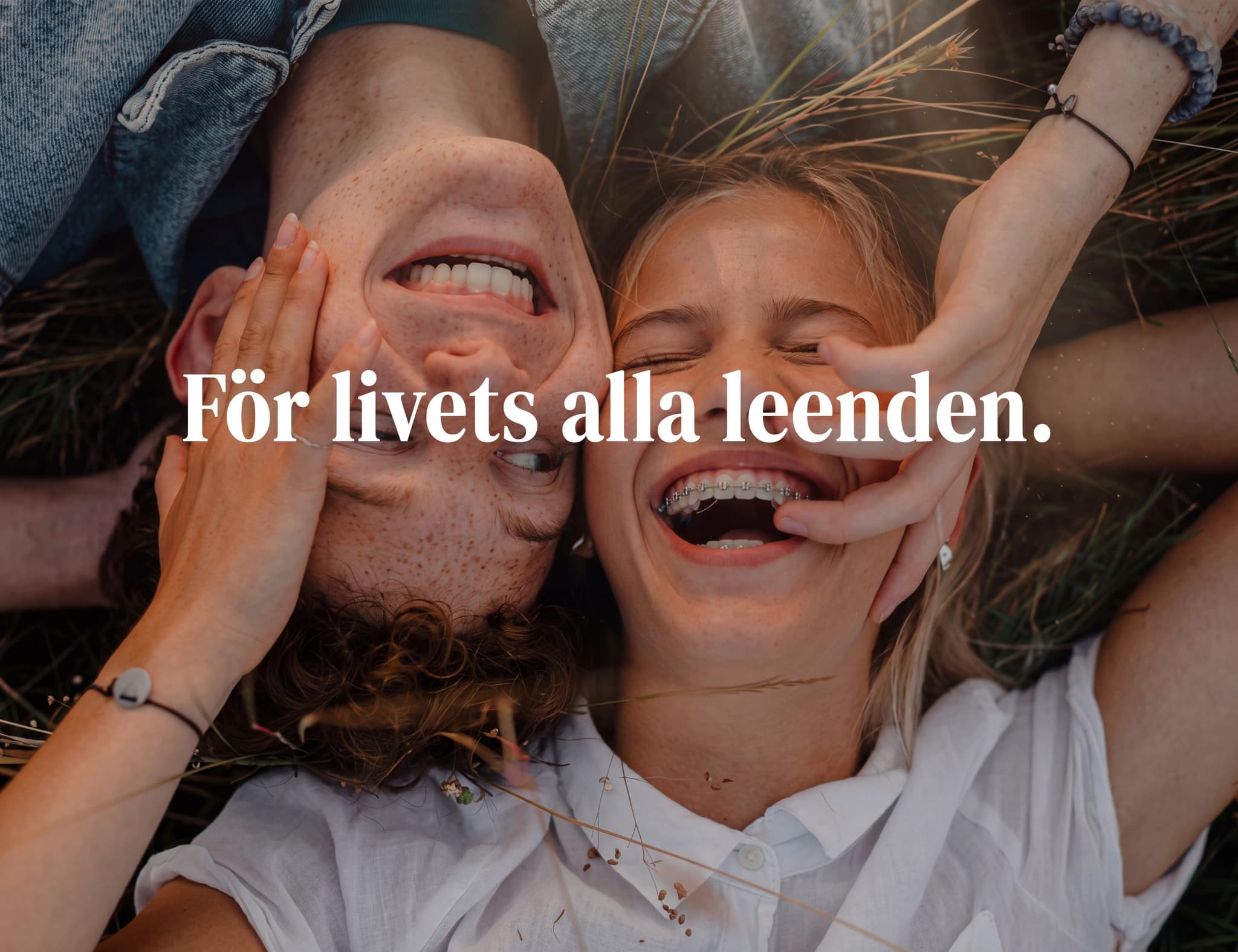 Ett ungt par som ligger ner utomhus och skrattar, med texten 'För livets alla leenden'.