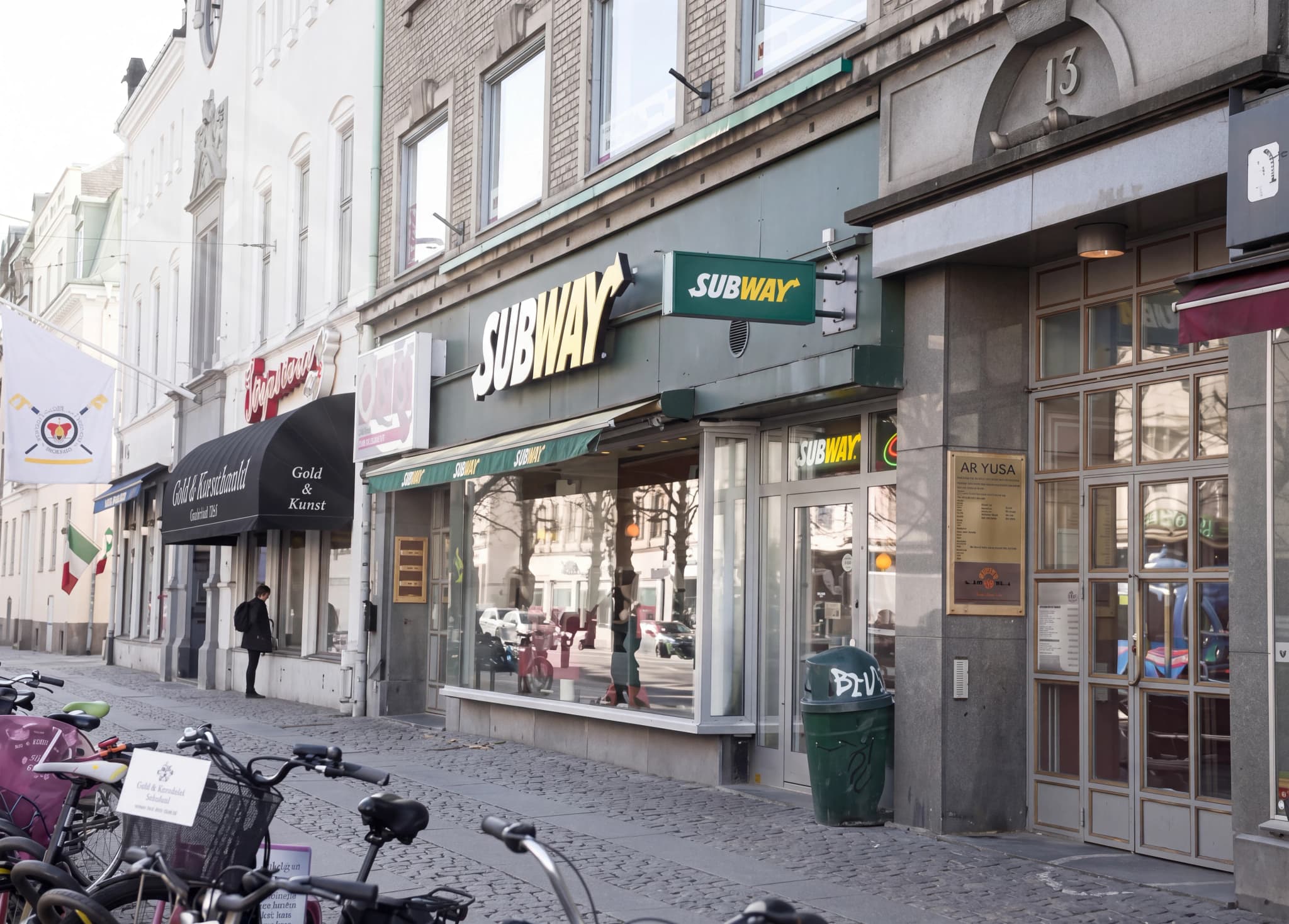 En fasadbild av en Subway-restaurang med gröna markiser och ett Subway-skylt, belägen på en stadsgata.