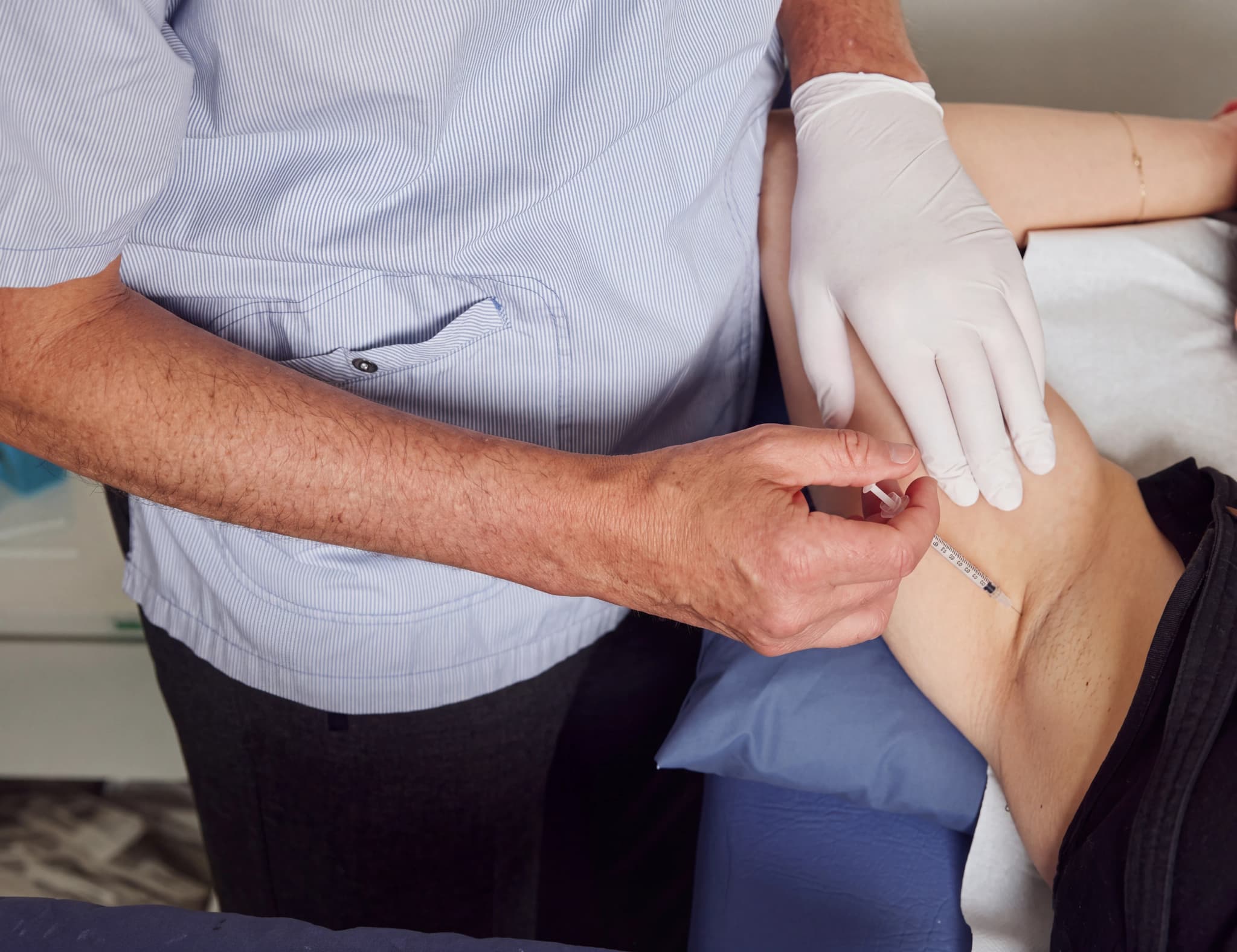 Läkare i handskar ger injektion i en patients arm.