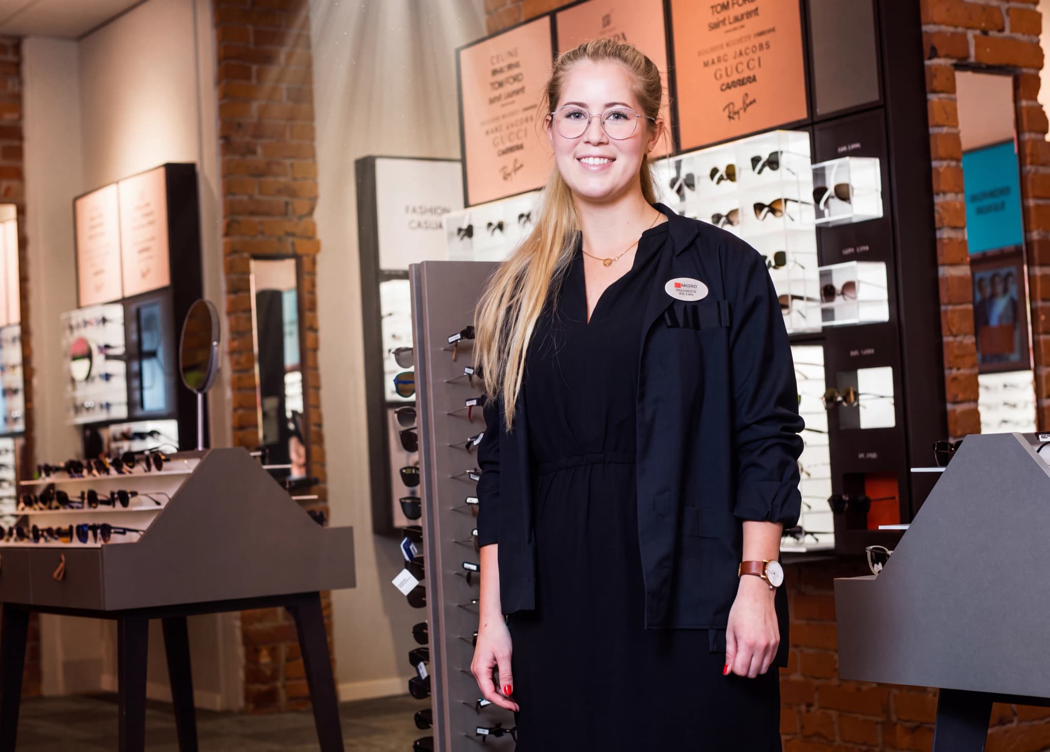 En ung kvinna med glasögon står i en optikbutik och ler mot kameran.