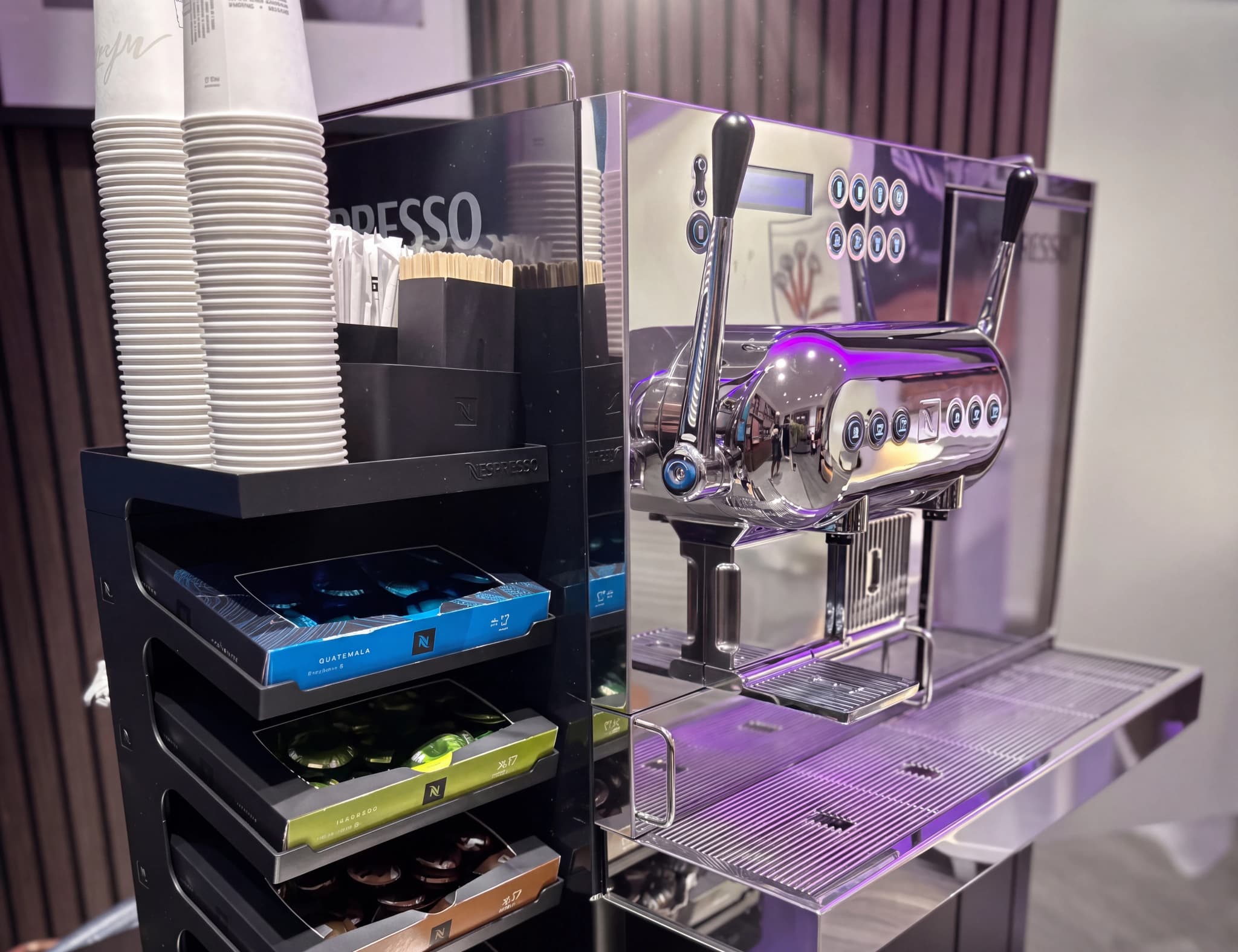 En Nespresso kaffemaskin med staplade pappersmuggar, kaffekapslar och tillbehör i en närbild.