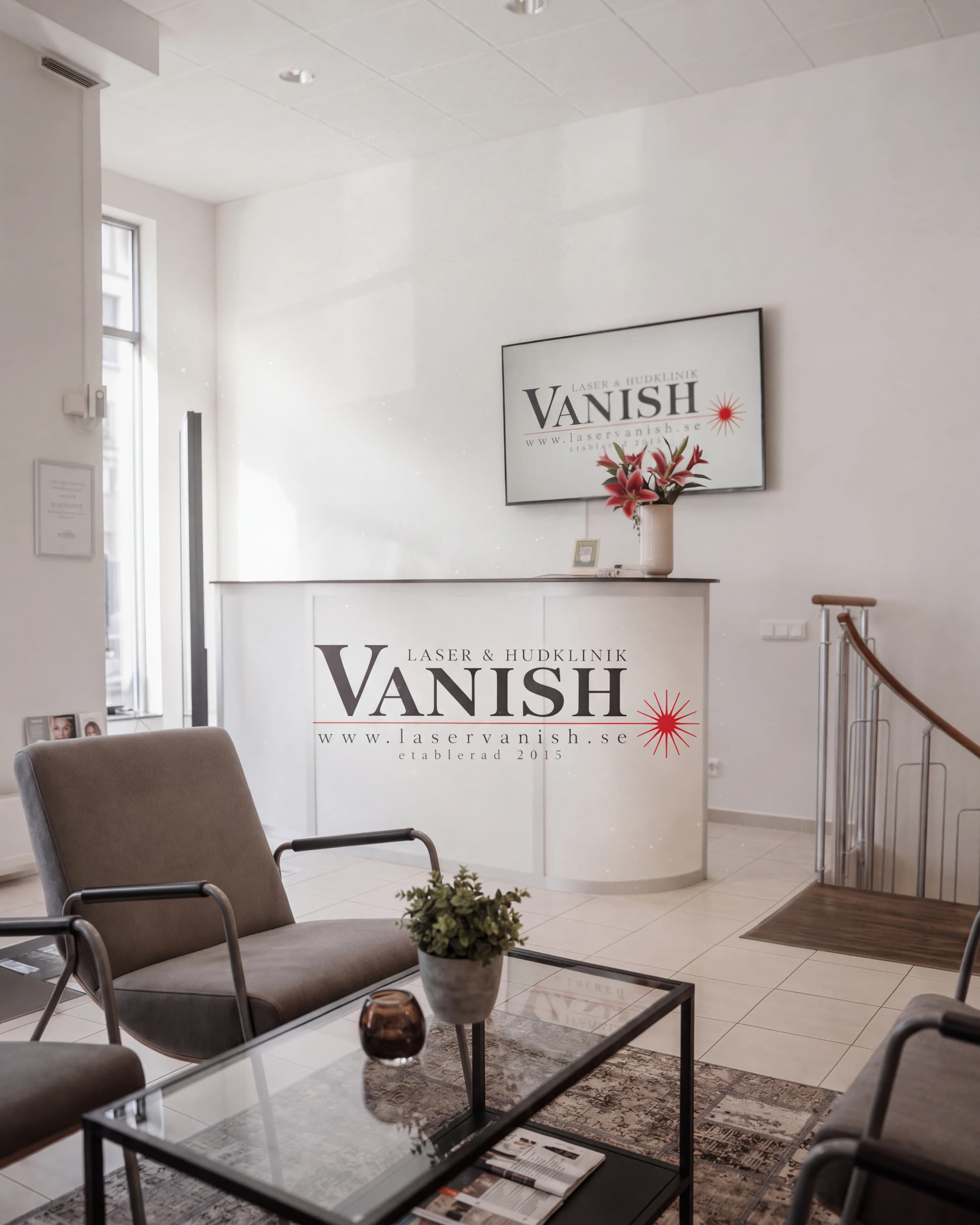 Väntrum och reception på Vanish klinik med bekväma sittplatser, ett glasbord och en reception med klinikens logotyp.
