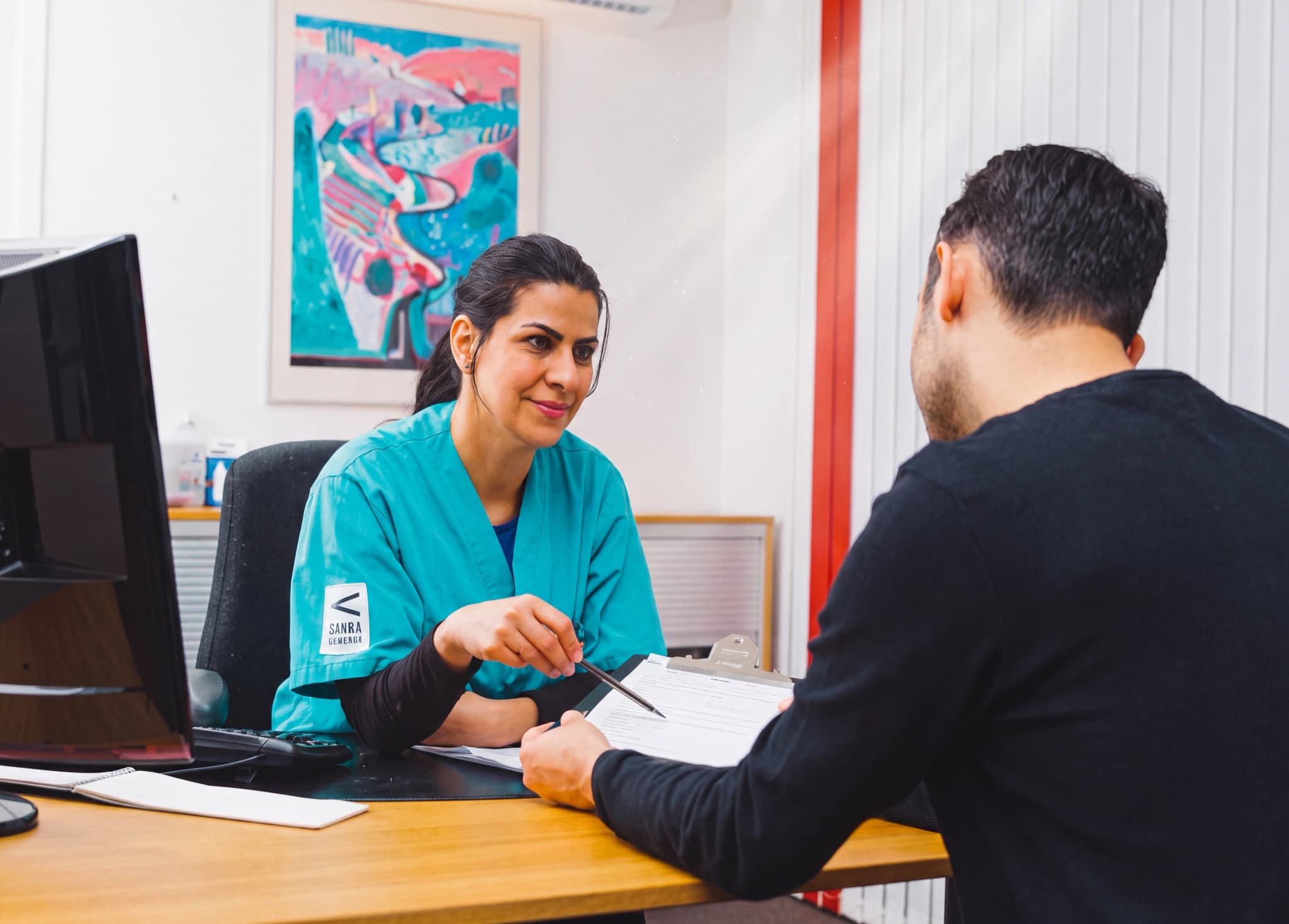Läkare i gröna kläder som diskuterar pappersarbete med en manlig patient vid ett skrivbord
