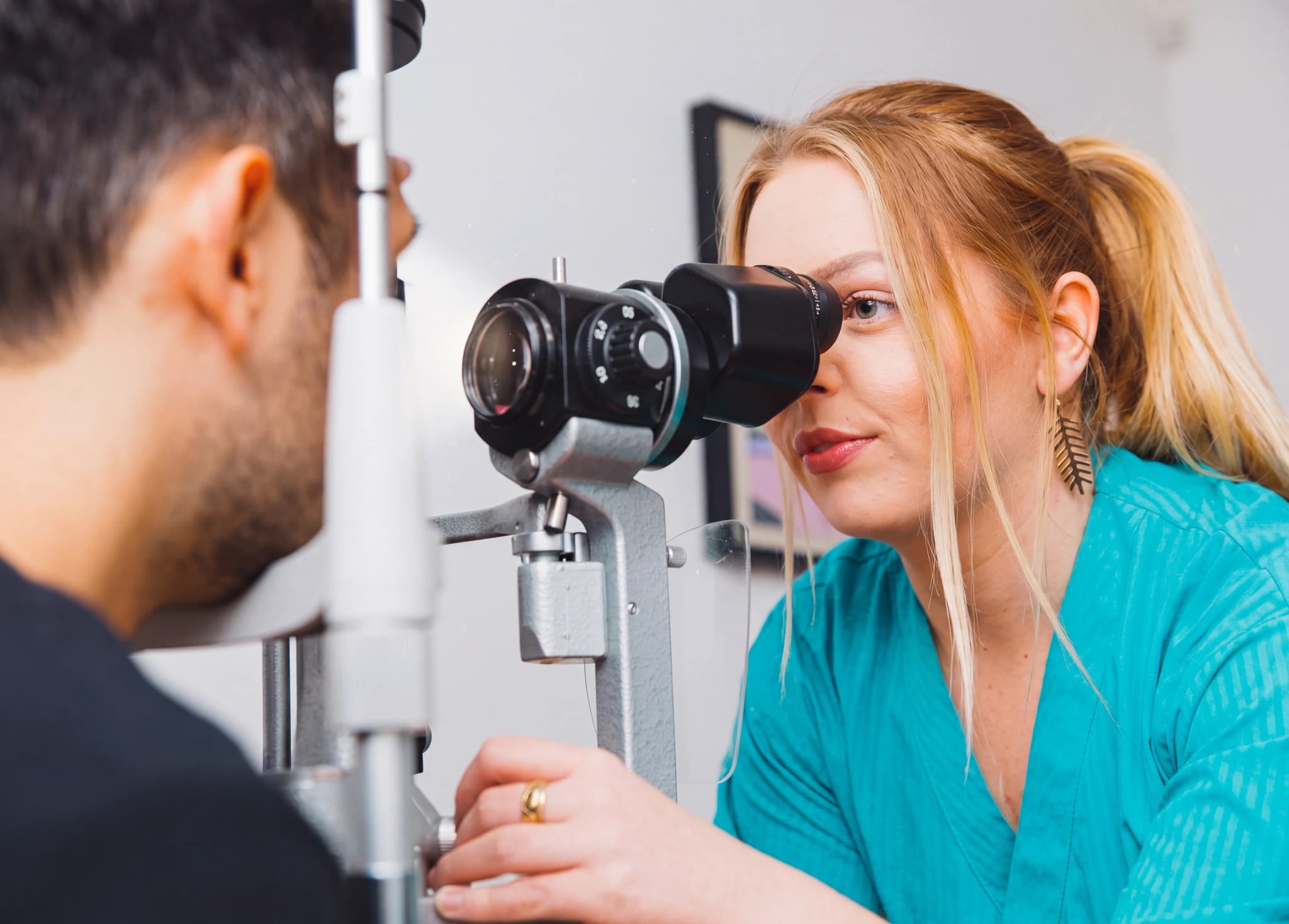 Optiker undersöker patientens öga med en spaltlampa i ett undersökningsrum.