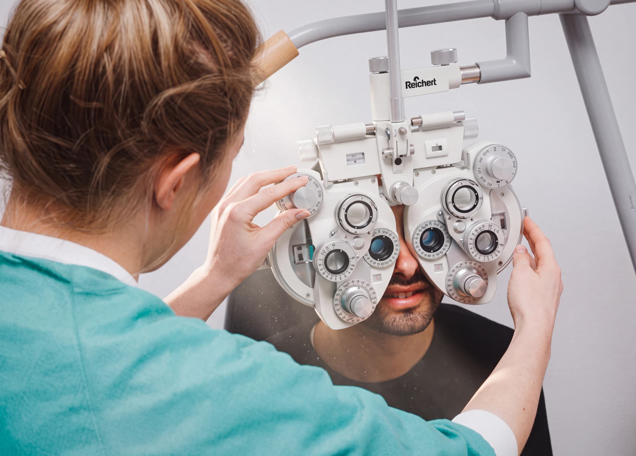 Optiker undersöker patientens ögon med en phoropter i ett undersökningsrum.
