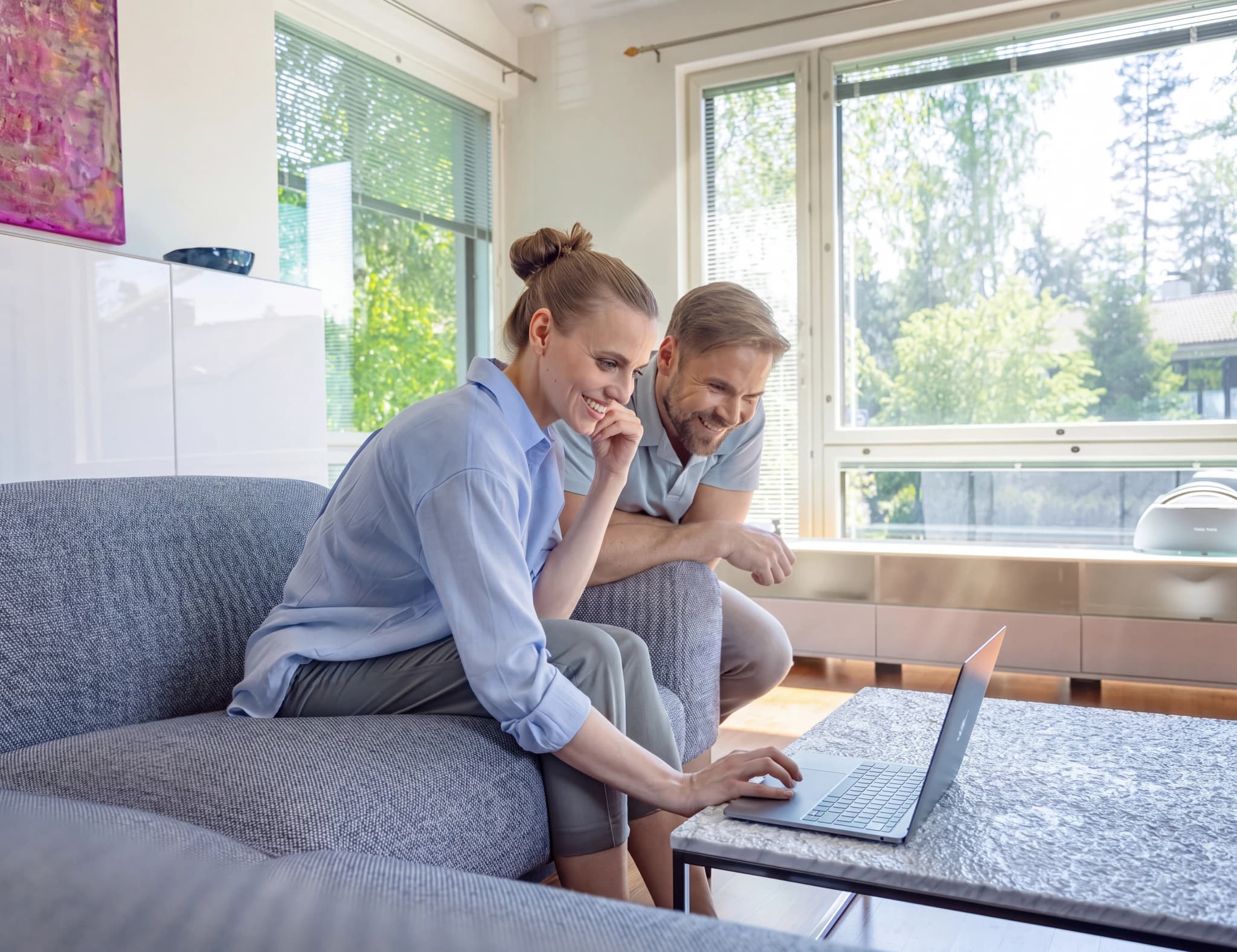 Ett leende par sitter i soffan och tittar på en laptop på vardagsrumsbordet.