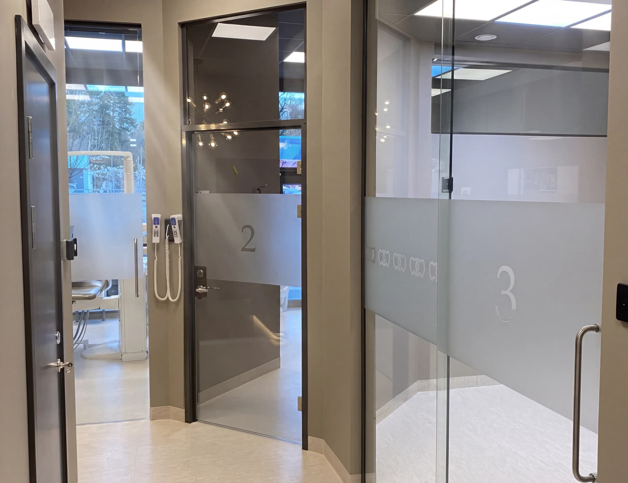 En korridor på en klinik med dörrar till behandlingsrum nummer 2 och 3. Dörrarna har frostat glas med nummer på.