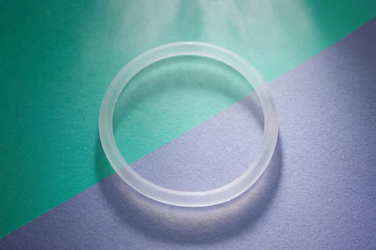 Ett ljusvitt, genomskinligt ringformat medicinskt hjälpmedel ligger på en bakgrund uppdelad diagonalt i turkos och lila.