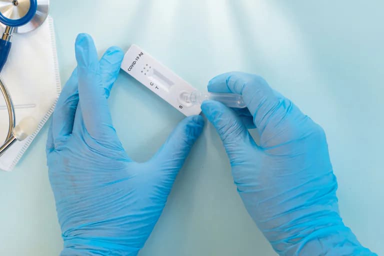 Händer i blåa handskar håller ett COVID-19 snabbtestkit med ett uppdraget teströr.