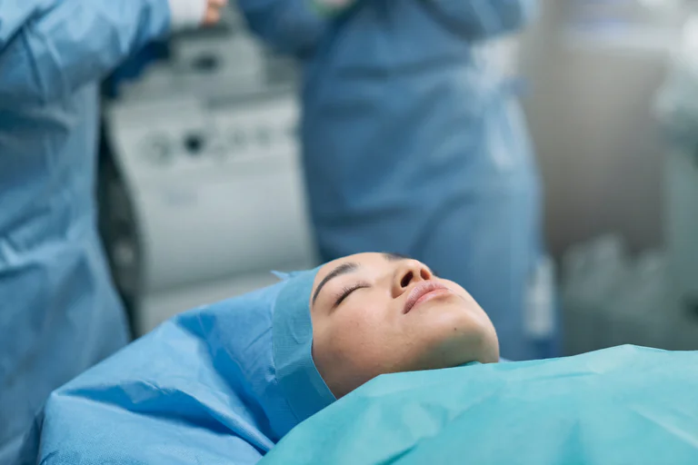 Patient som ligger på ett operationsbord, förberedd för operation med blå operationskläder och skyddshuva.