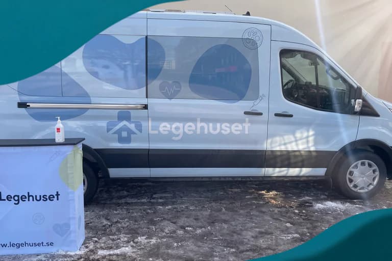 En ljusblå mobil klinikbil med Legehuset-logotyp och medicinska ikoner på sidan, parkerad utomhus med en informationsdisk framför.