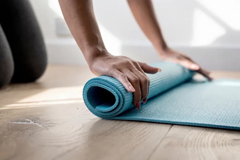 Person som rullar ihop en blå yogamatta på ett trägolv.