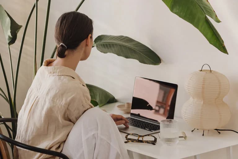 Person som arbetar på en laptop vid ett skrivbord med en skrivbordslampa och glas vatten.