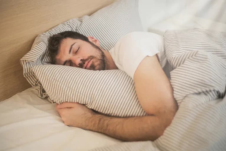Man sover bekvämt i en säng med randiga lakan och kudde.
