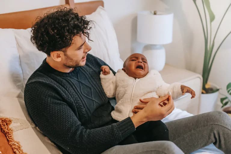Pappa tröstar sitt gråtande spädbarn i en inomhusmiljö.