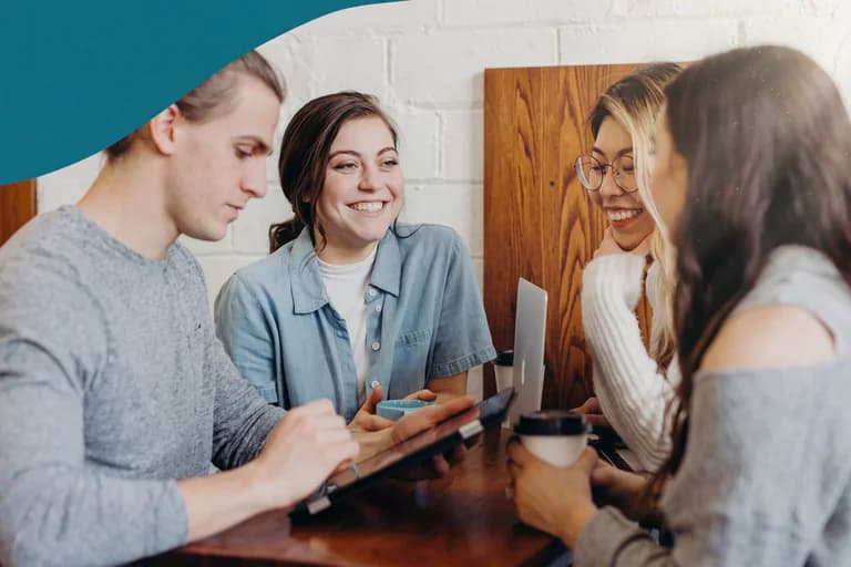En grupp på fyra unga vuxna av olika etnicitet samlade runt ett bord på ett kafé och diskuterar något på en surfplatta.