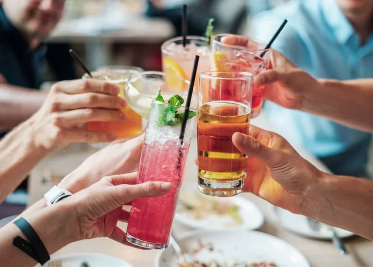 En grupp människor skålar med färgglada drinkar runt ett bord på en restaurang.
