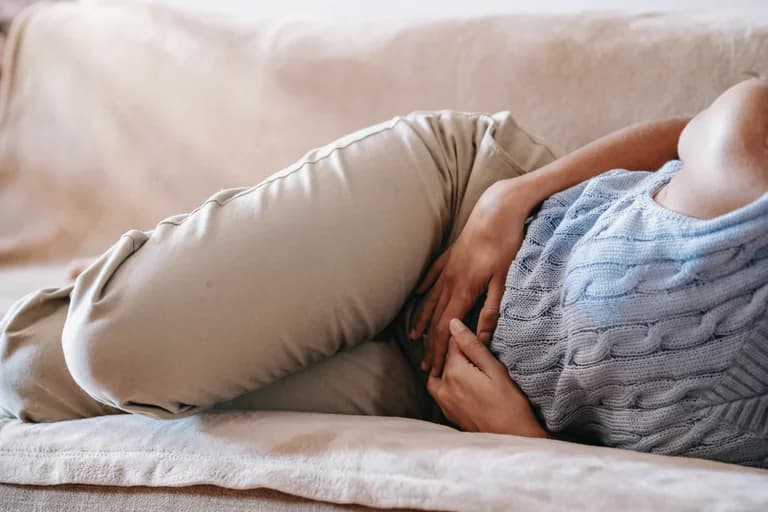 En person ligger hopkrupen på en soffa med händerna på magen, möjligen på grund av magsmärtor.