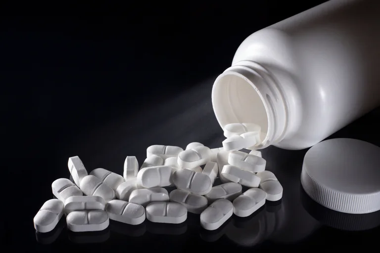Vita piller som hälls ut ur en vit medicinflaska mot en mörk bakgrund.