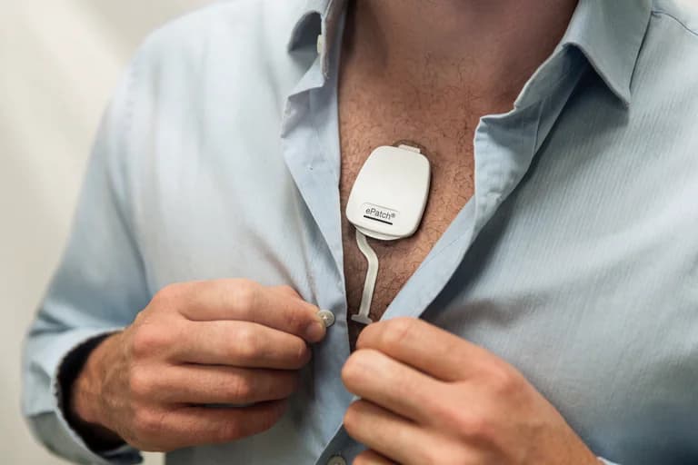 Man som knäpper skjortan och har ett ePatch hjärtövervakningsplåster på bröstet.