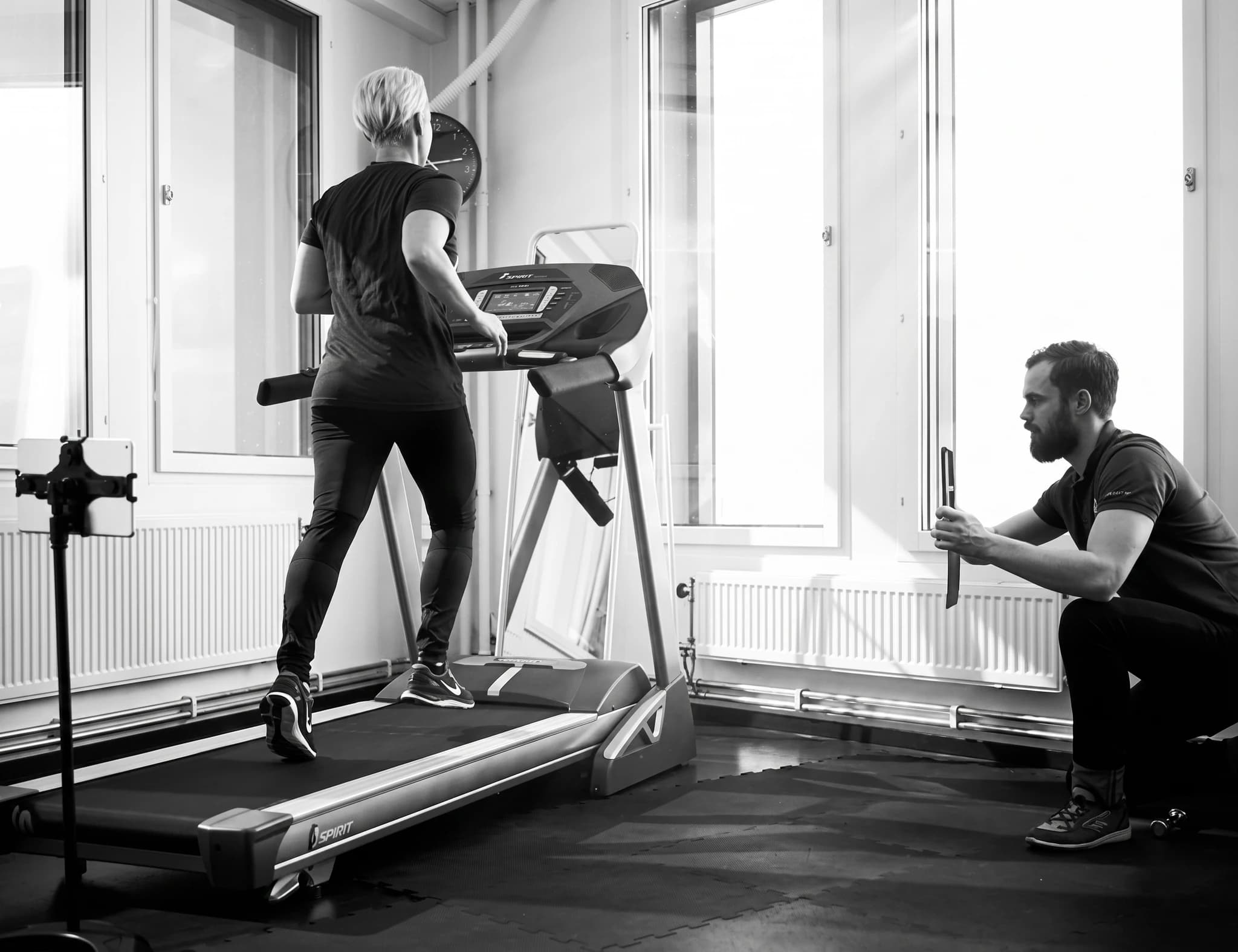 Kvinna springer på ett löpband i en tränings- och rehabiliteringsklinik, medan en man sitter bredvid och observerar.