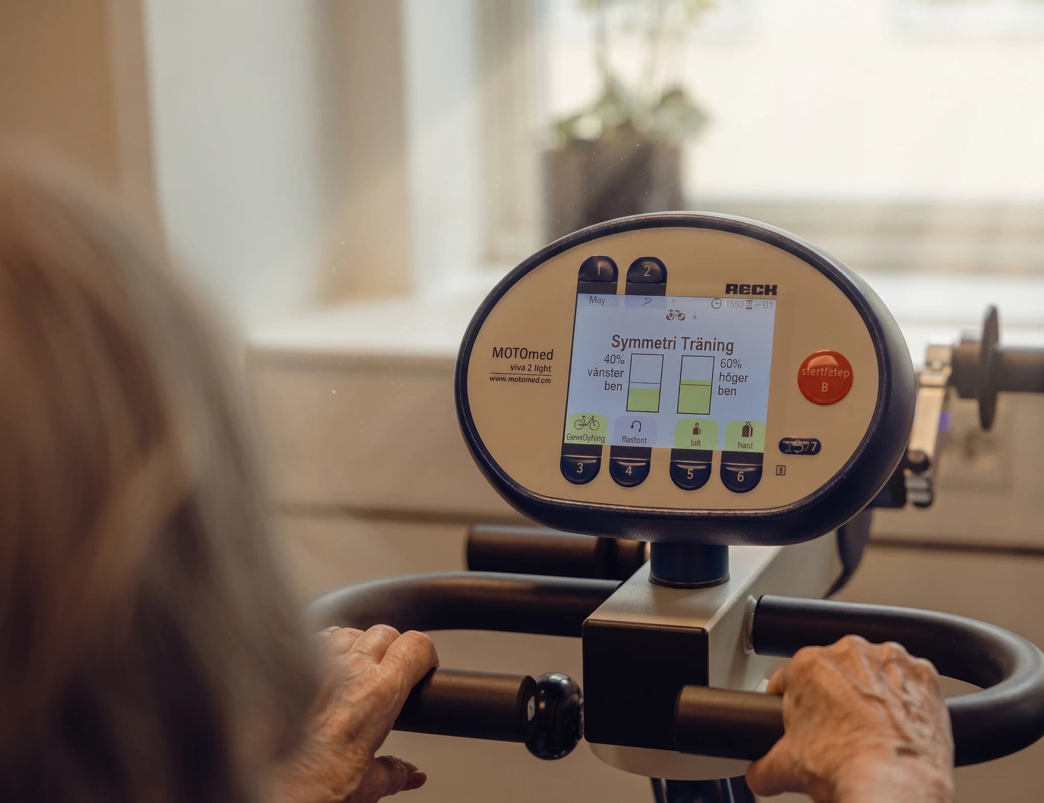 Äldre person som använder en rehabiliteringsmaskins skärm med träningsprogram och symmetrimätning.
