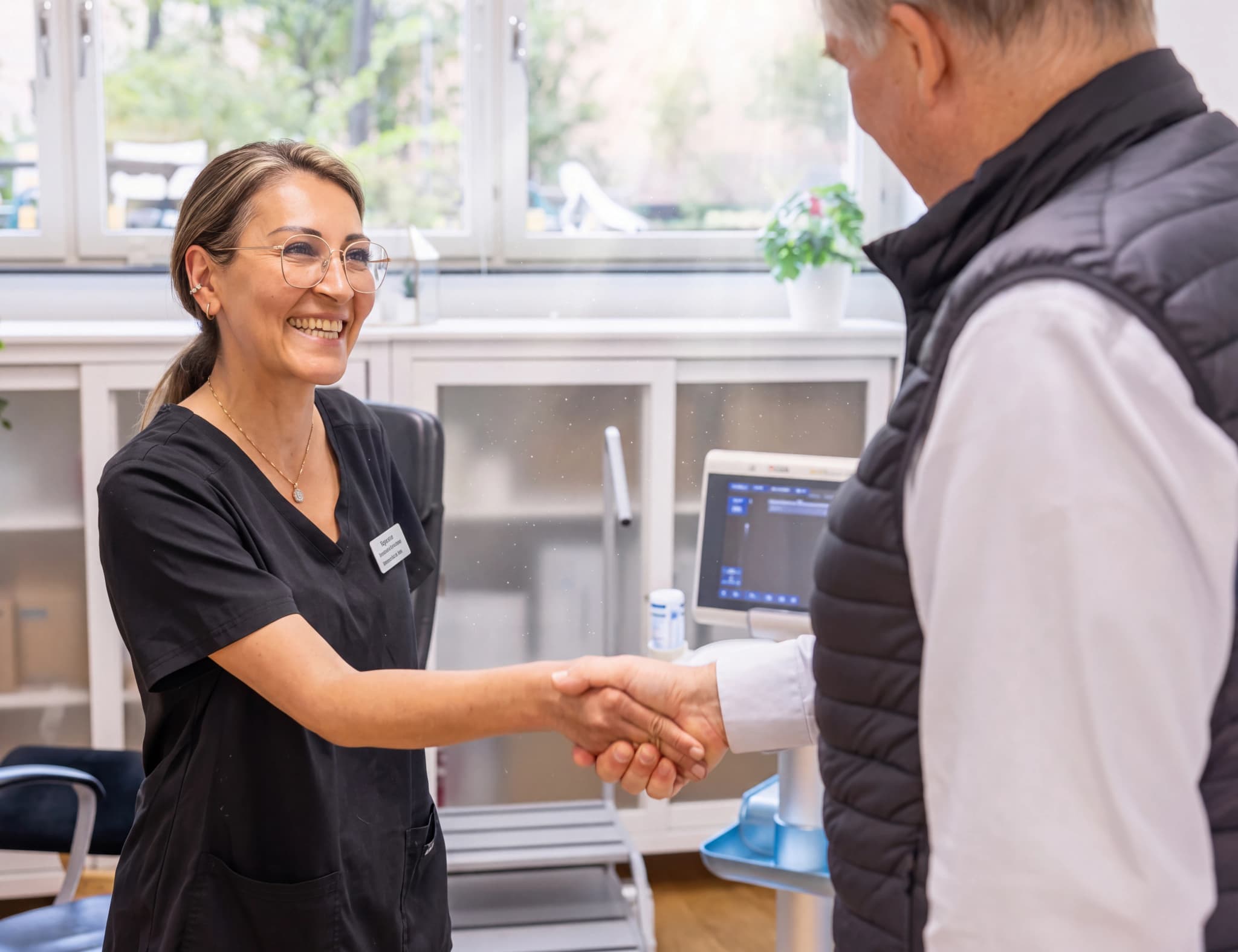 Läkare i svarta arbetskläder skakar hand med en manlig patient vid en ultraljudsmaskin i ett undersökningsrum.